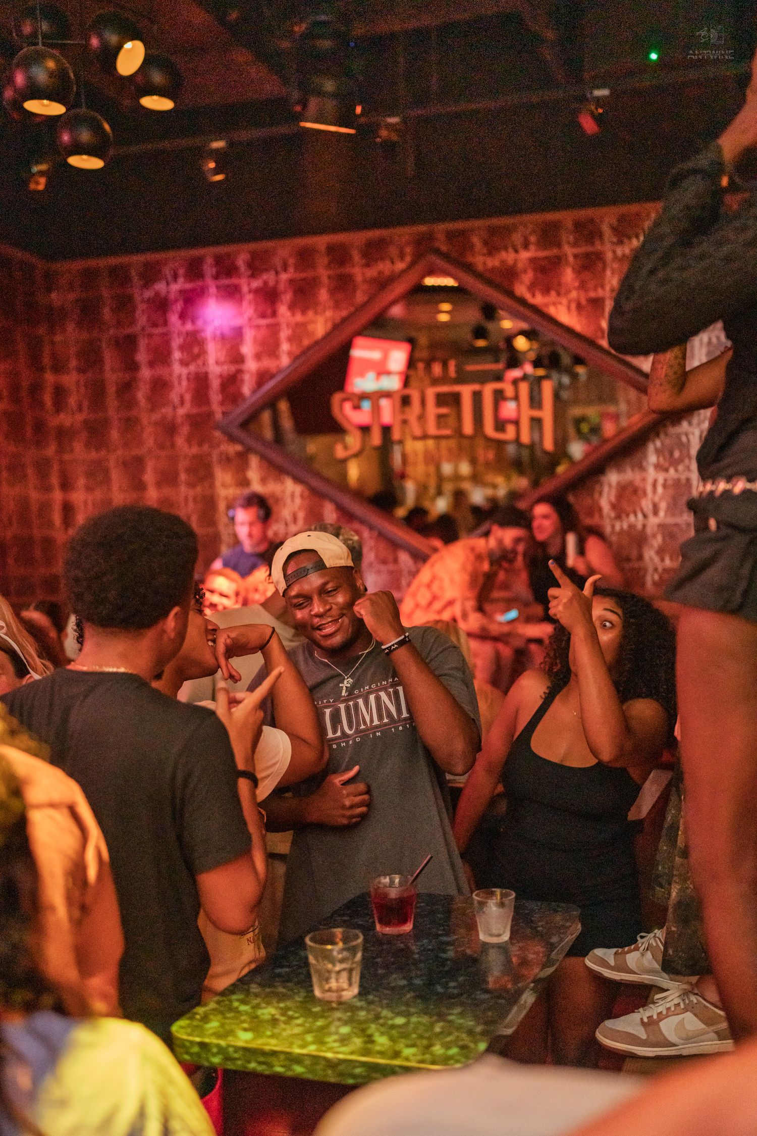 Man posing and smiling at The Stretch nightclub surrounded by friends and drinks.