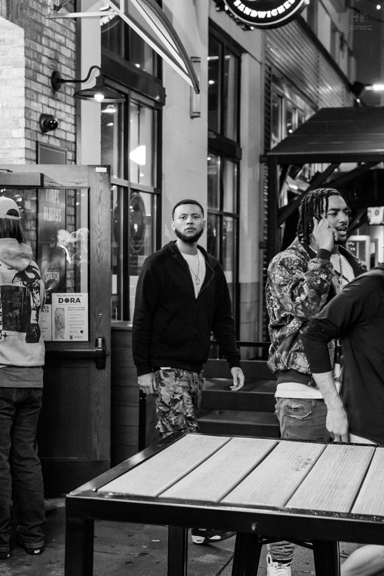Young men standing outside a bar on a city street at night.