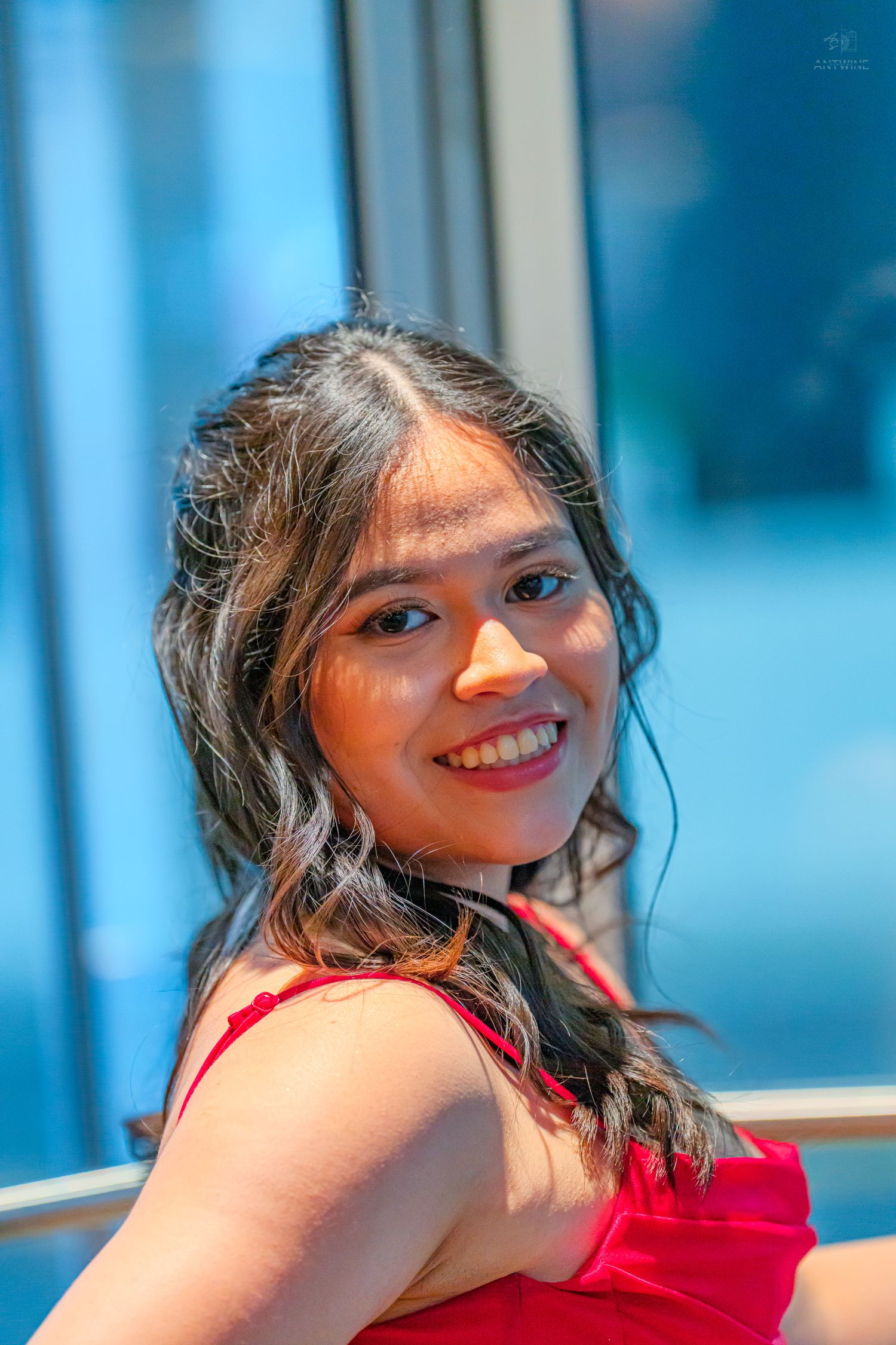 Smiling young woman with long dark hair wearing a red dress, posing against a blue background.
