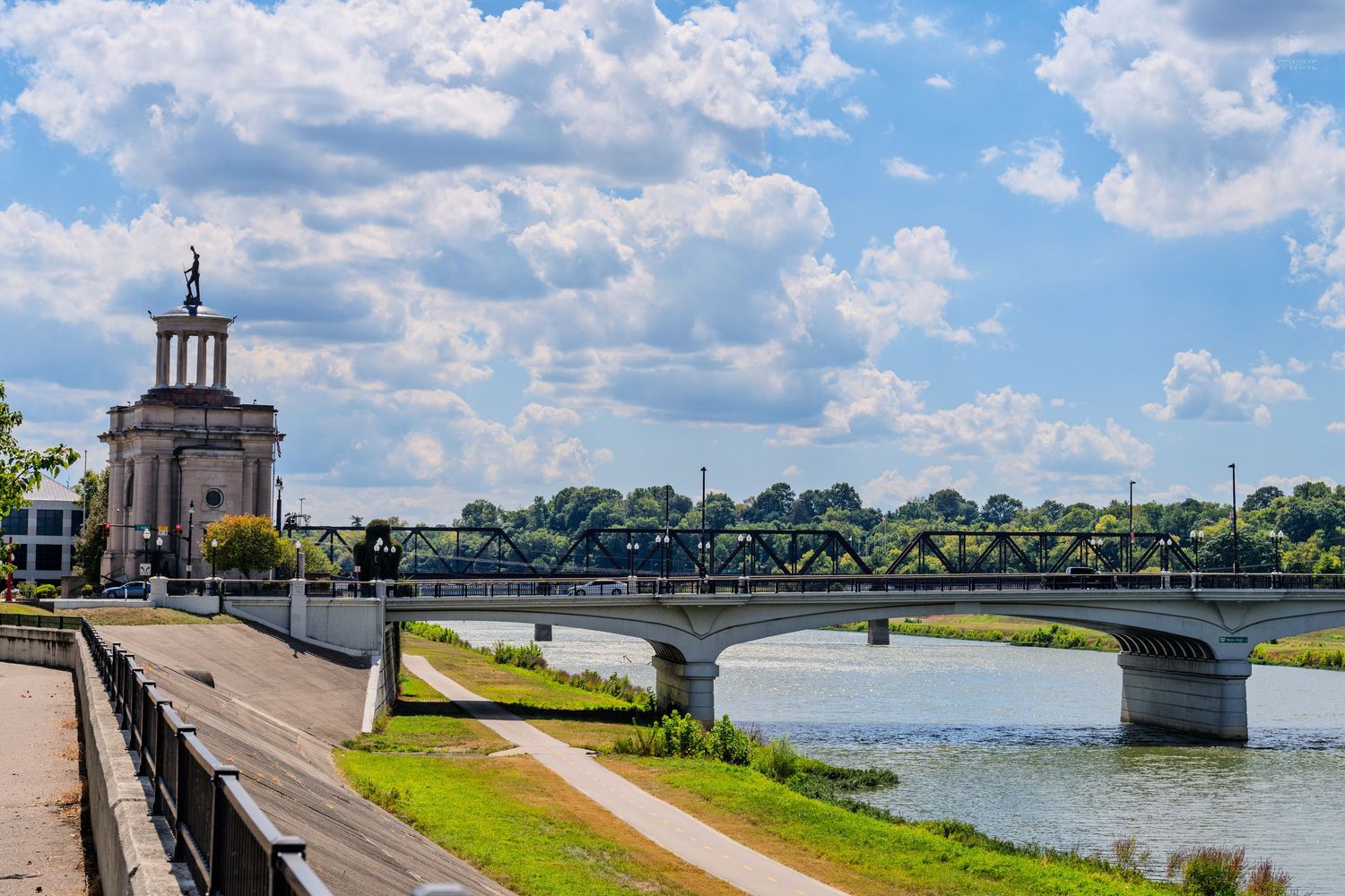 Historic bridge and classical tower building along a scenic river under a partly cloudy sky.