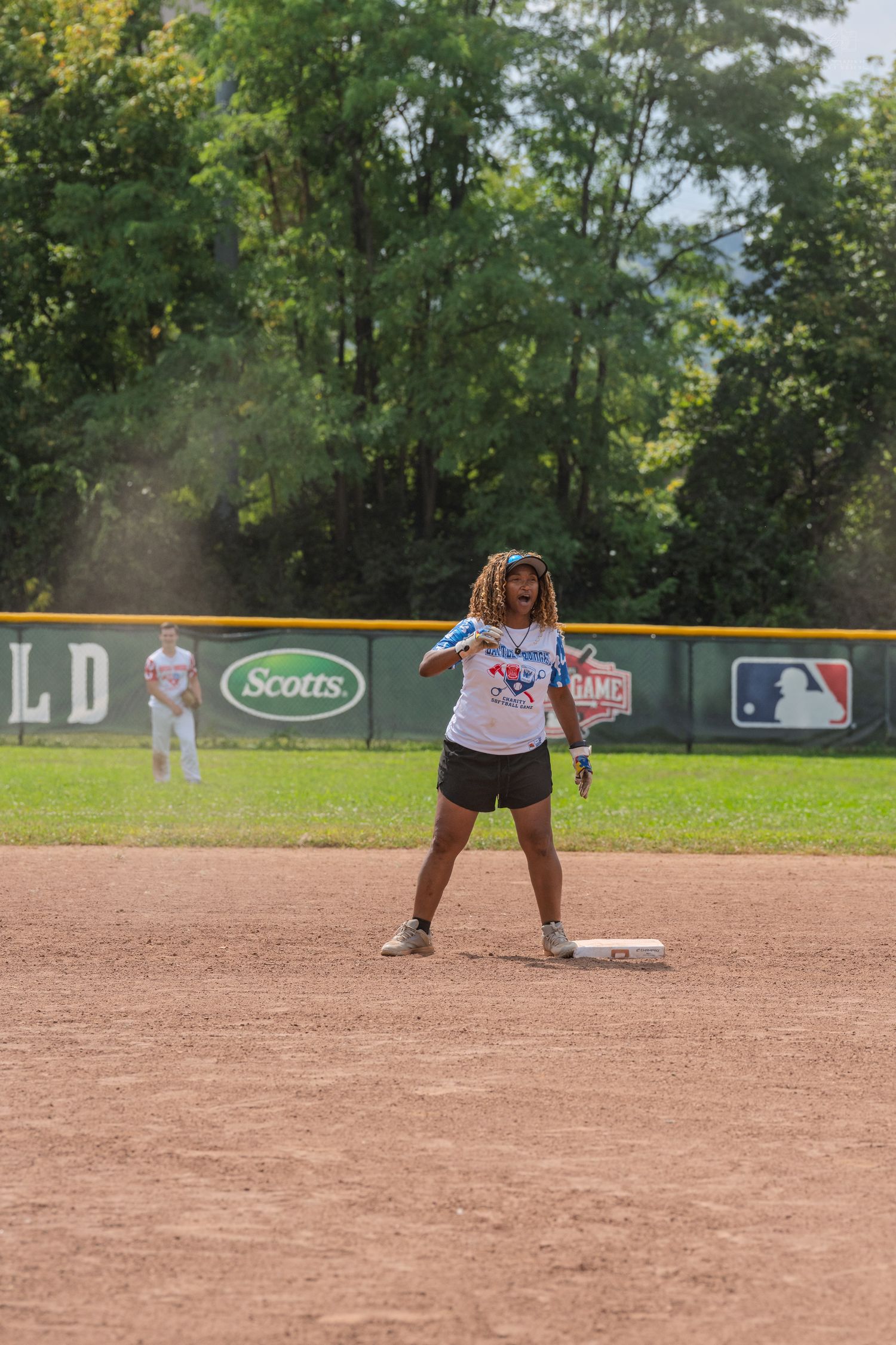 A female softball player celebrates at second base during a sunny outdoor game at a Scotts-sponsored field.
