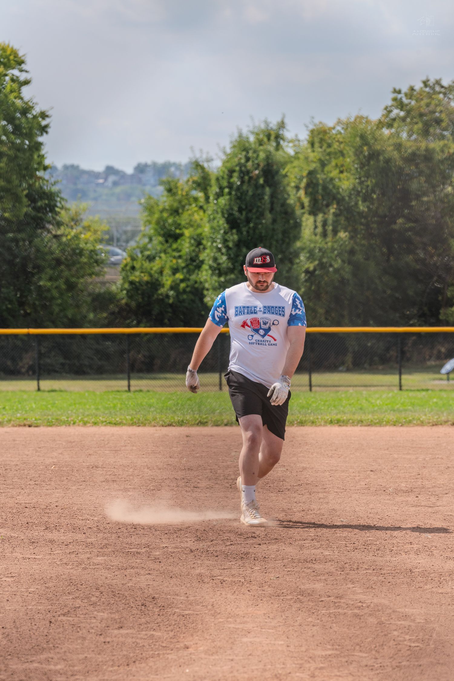 Male softball player runs bases in matching team jersey during an outdoor game on a dirt field.