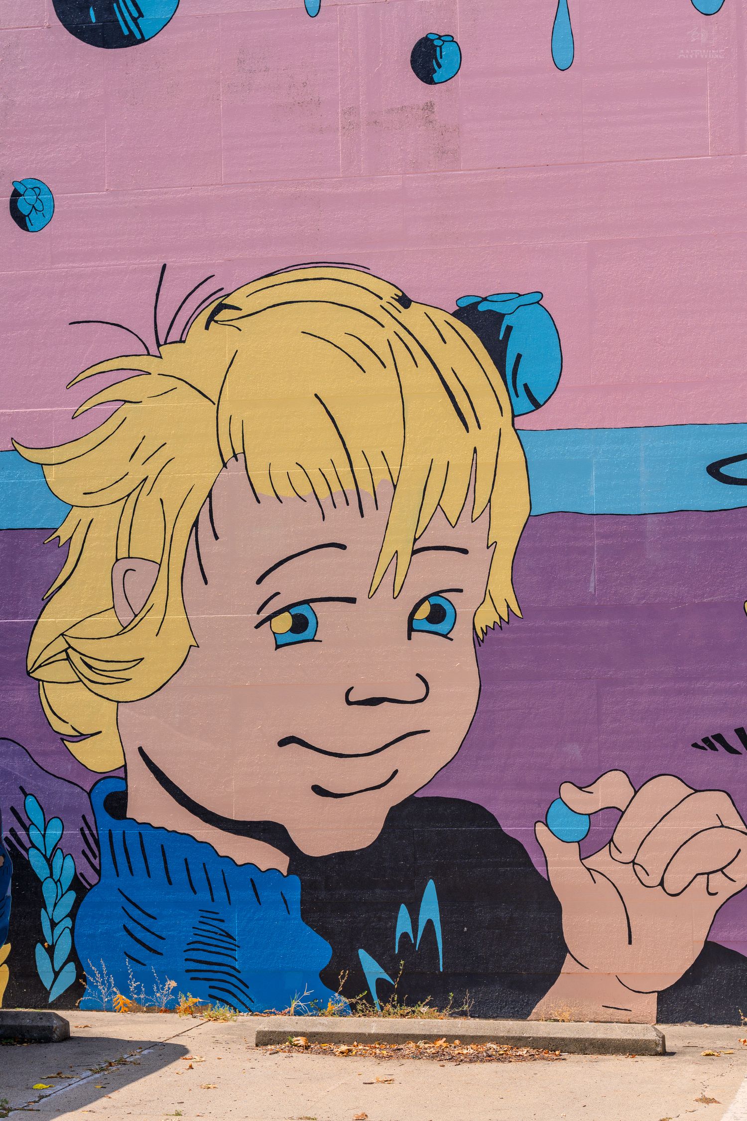 Colorful street art mural of a cartoon blonde child with blue eyes, painted on a pink and purple wall.