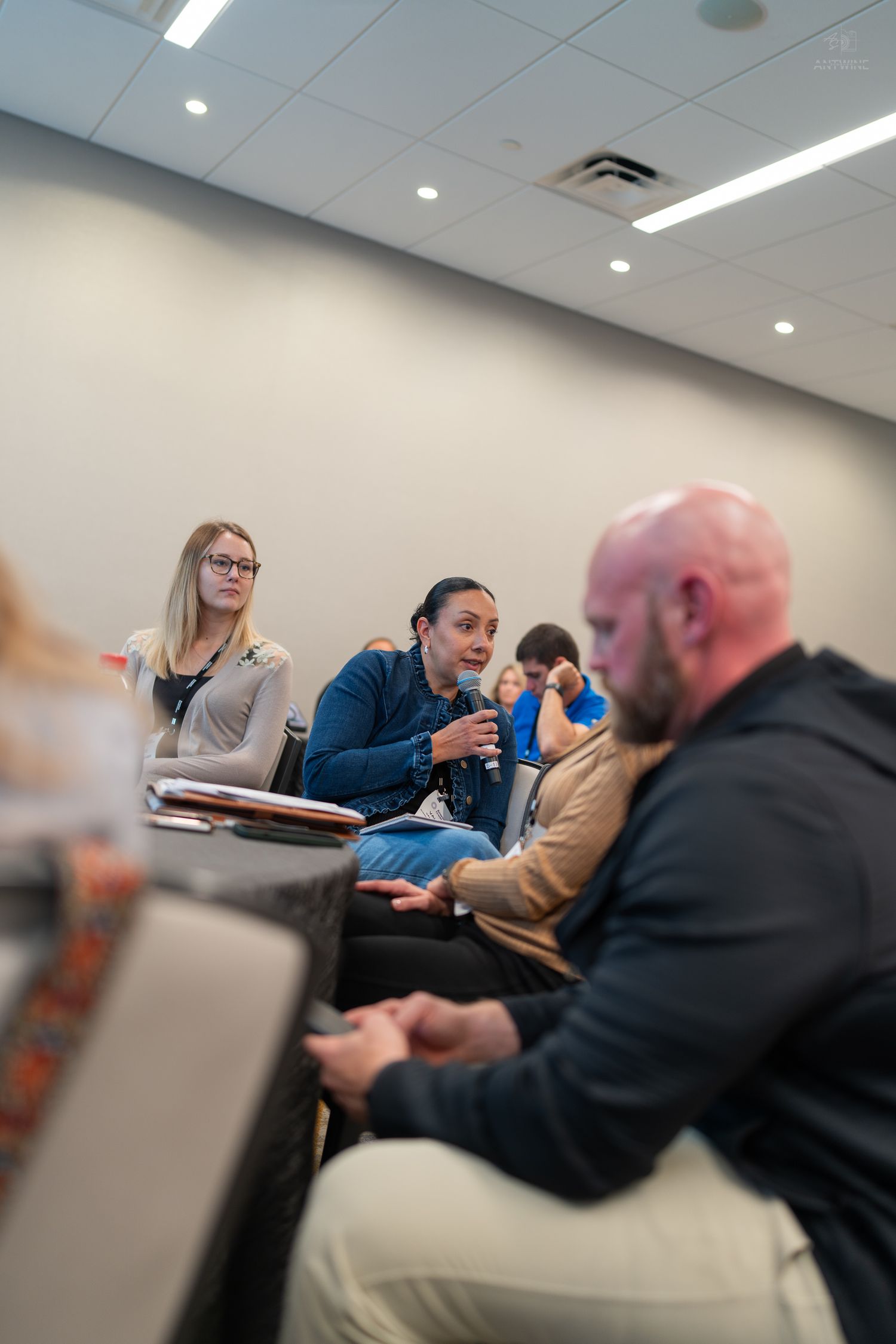A woman speaks into a microphone during a panel discussion in a modern conference room with attendees listening attentively.