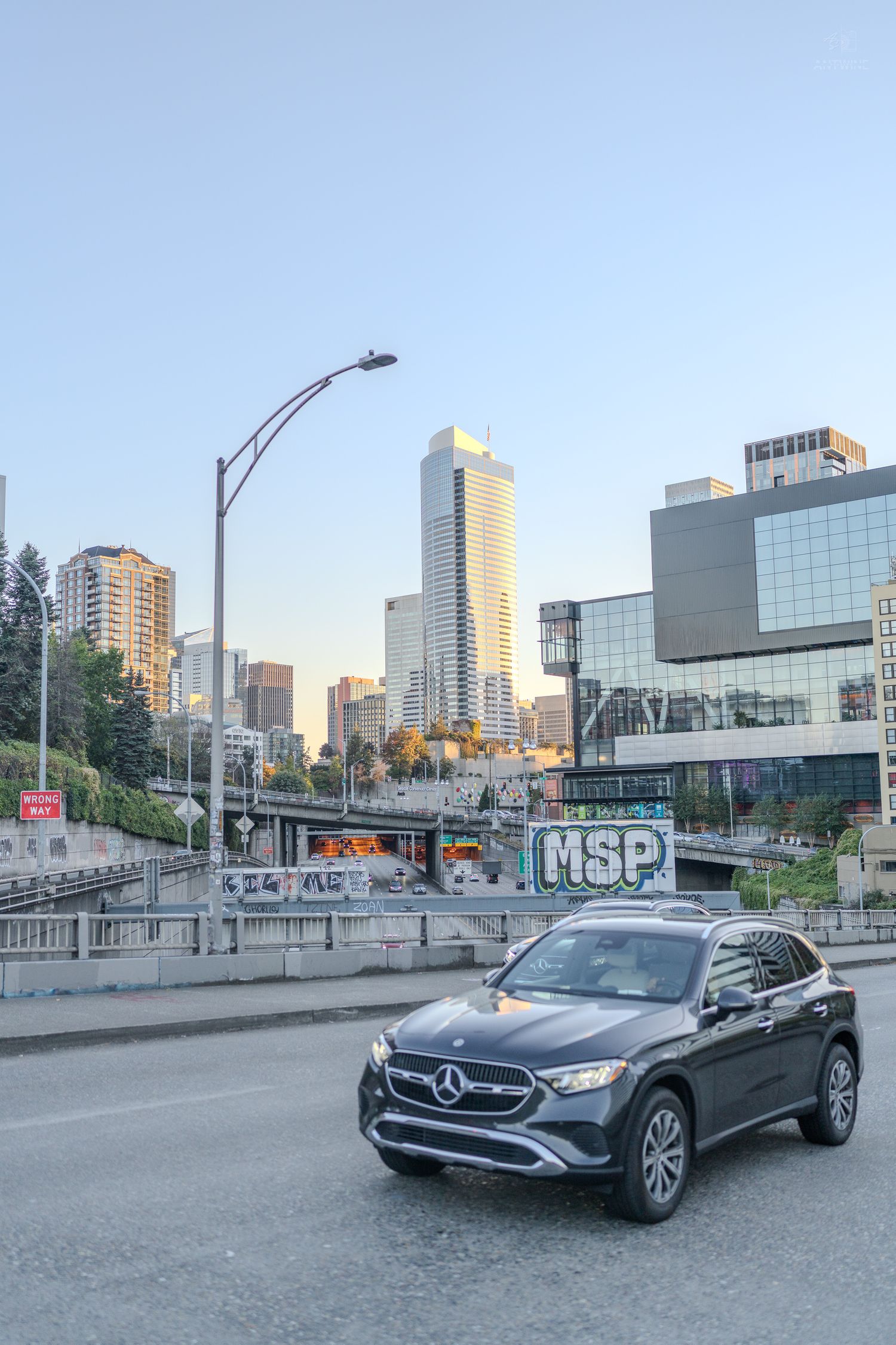 Dark blue Mercedes-Benz SUV on city road with Seattle skyline and MSP graffiti wall at dusk.