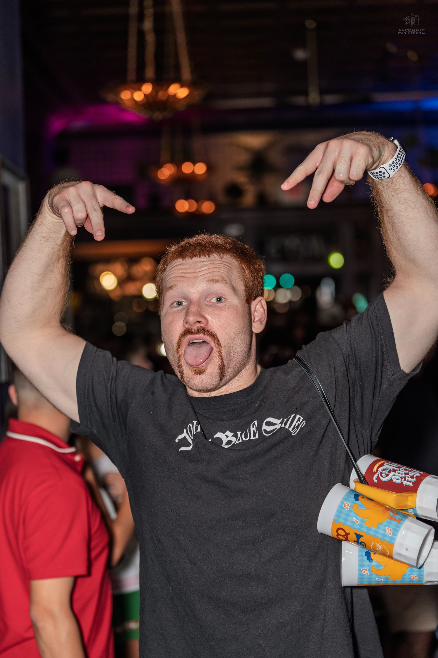 Energetic redhead man making a funny face with hands raised at a bar event.