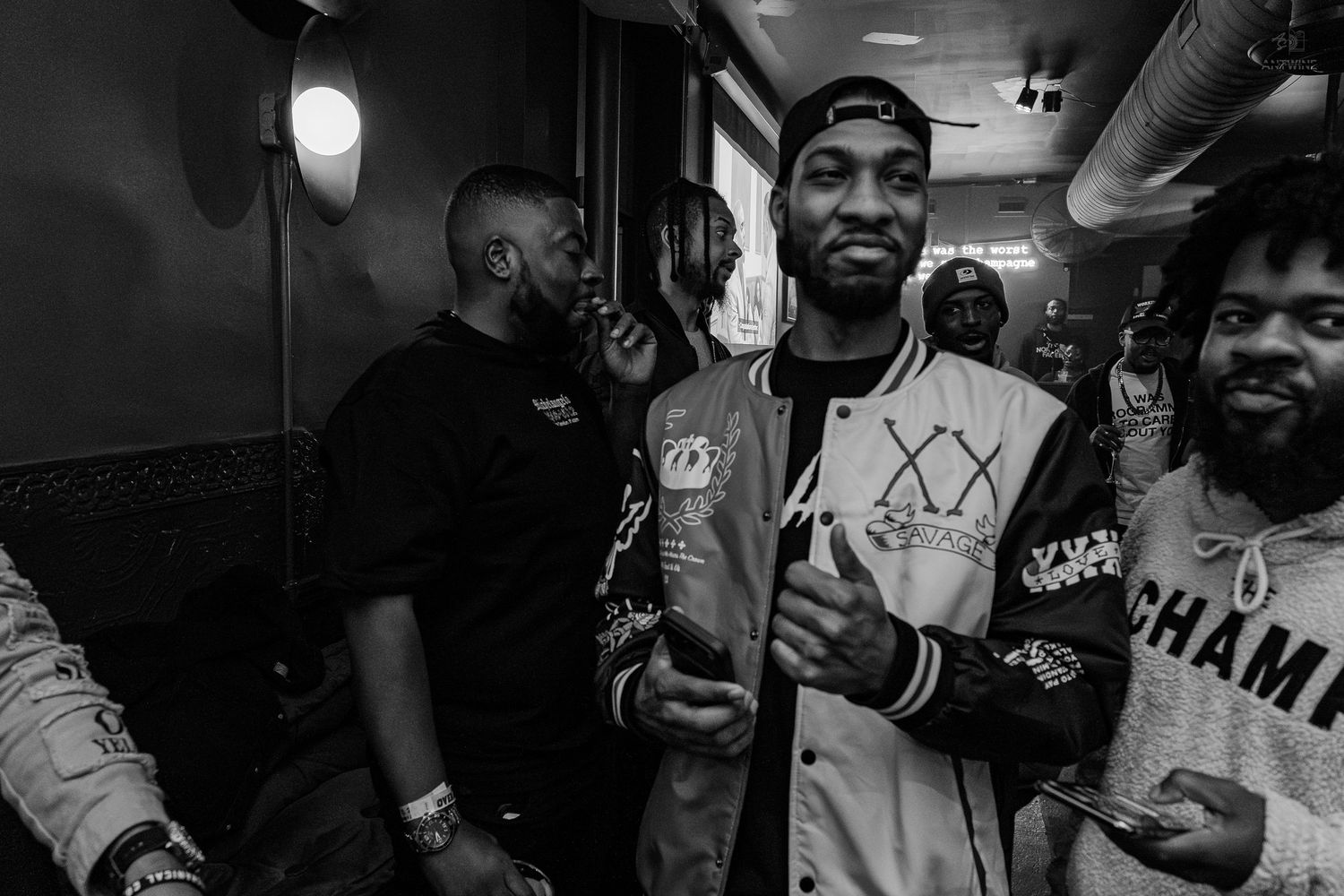 Black and white photo of men smiling and posing together at an indoor event, wearing stylish jackets and caps.