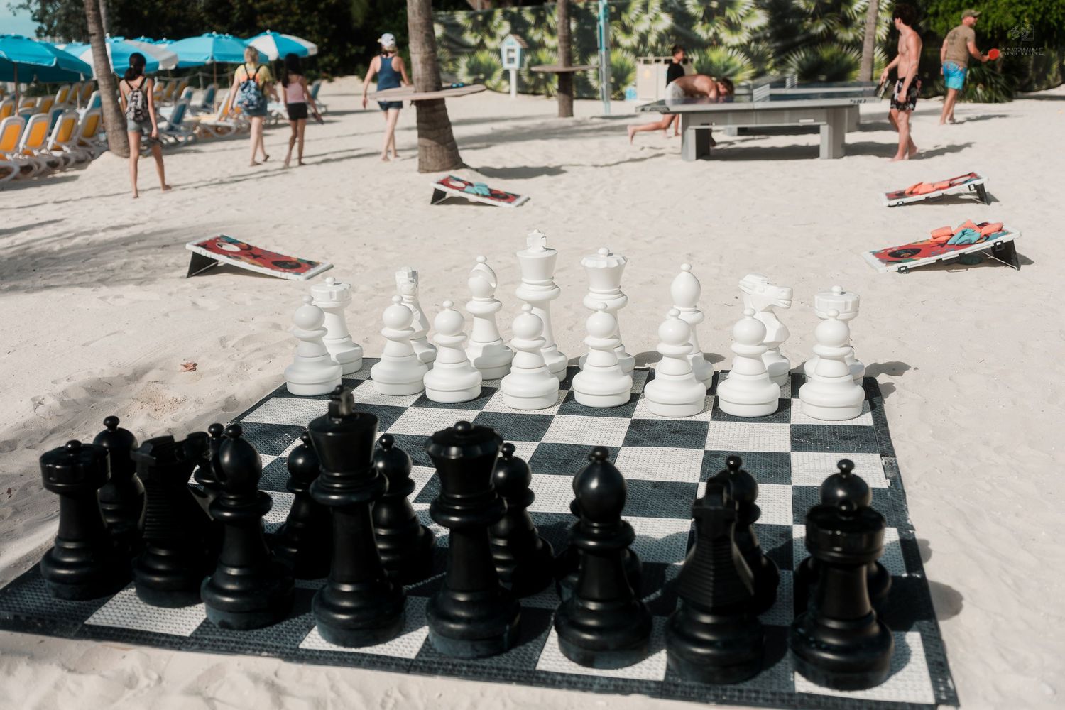 Giant outdoor chess set with black and white pieces on a sandy beach resort.