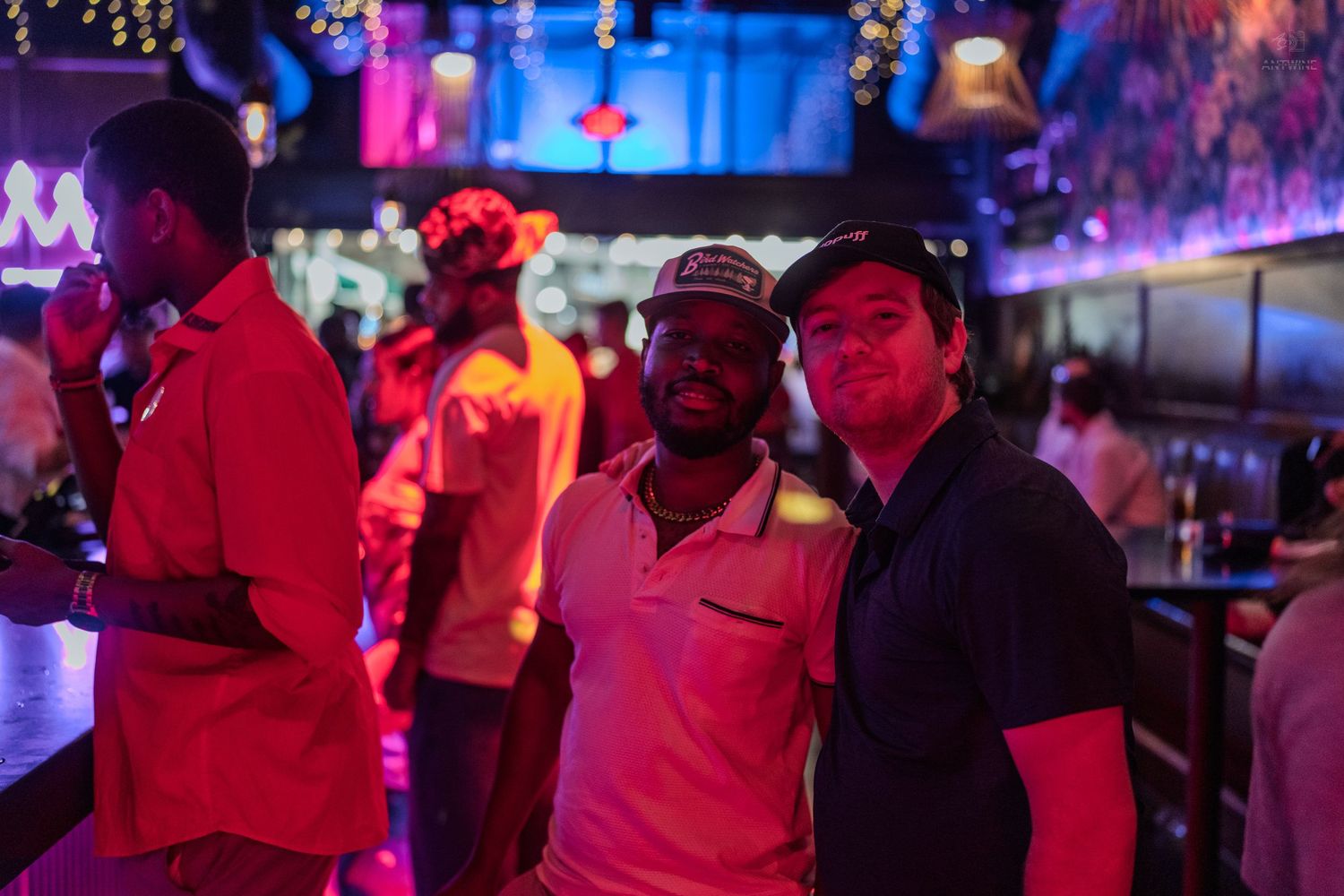 Two men posing together smiling in a purple neon-lit nightclub bar.