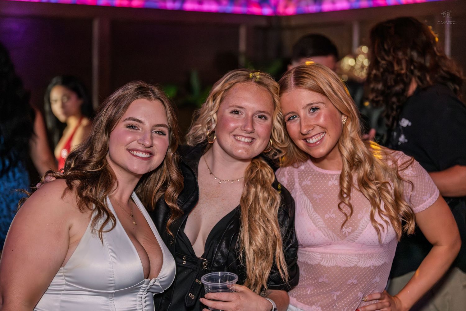 Three cheerful young women posing closely together at a lively nightclub party.