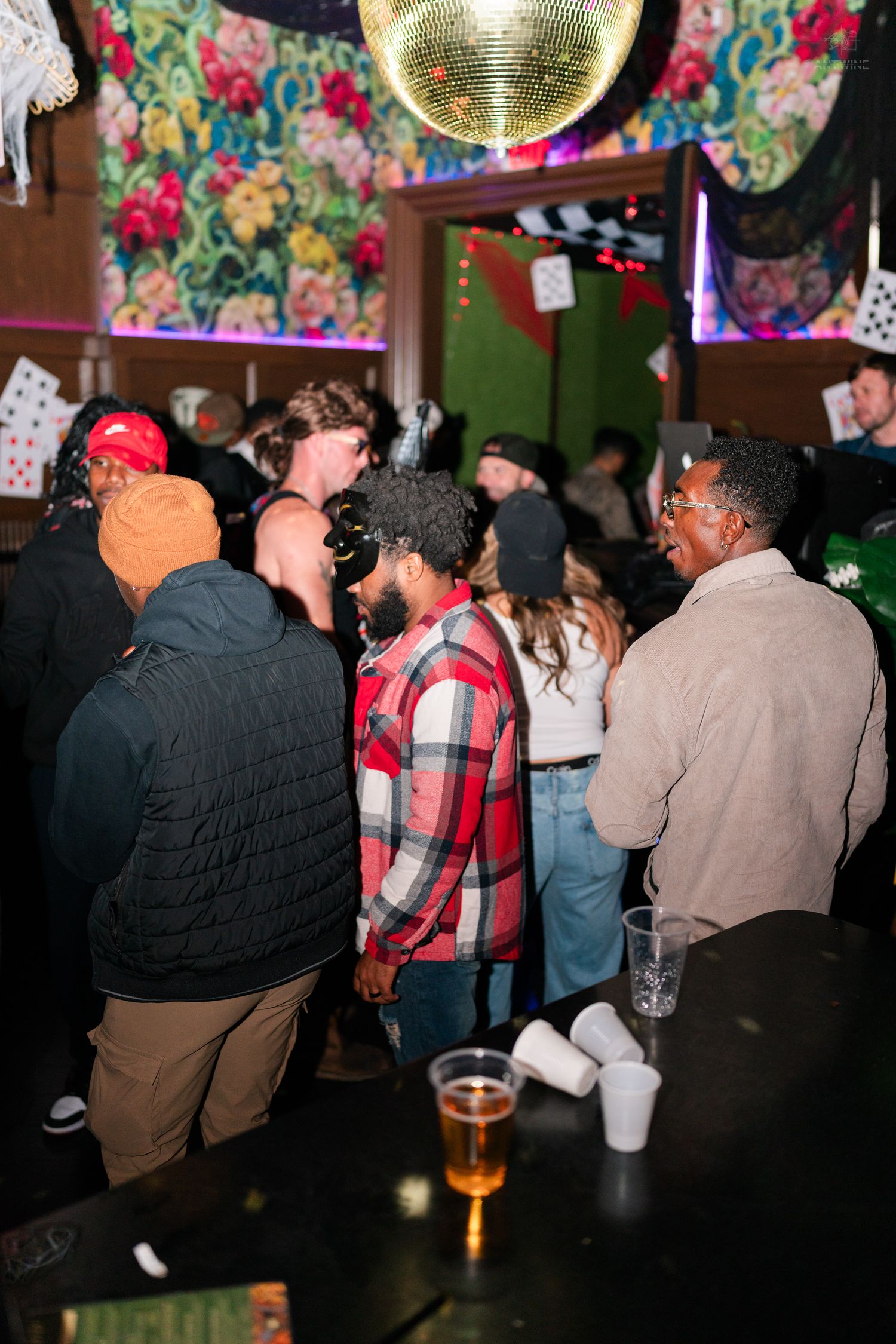 Group of partygoers socializing near a bar with a disco ball at a Halloween event.