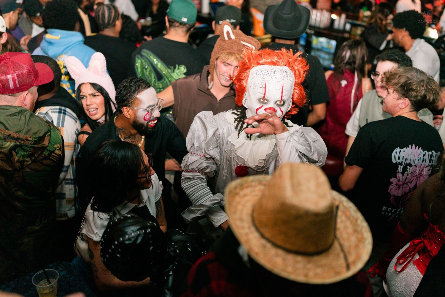 Halloween party crowd featuring a Pennywise clown costume among other festive partygoers indoors.