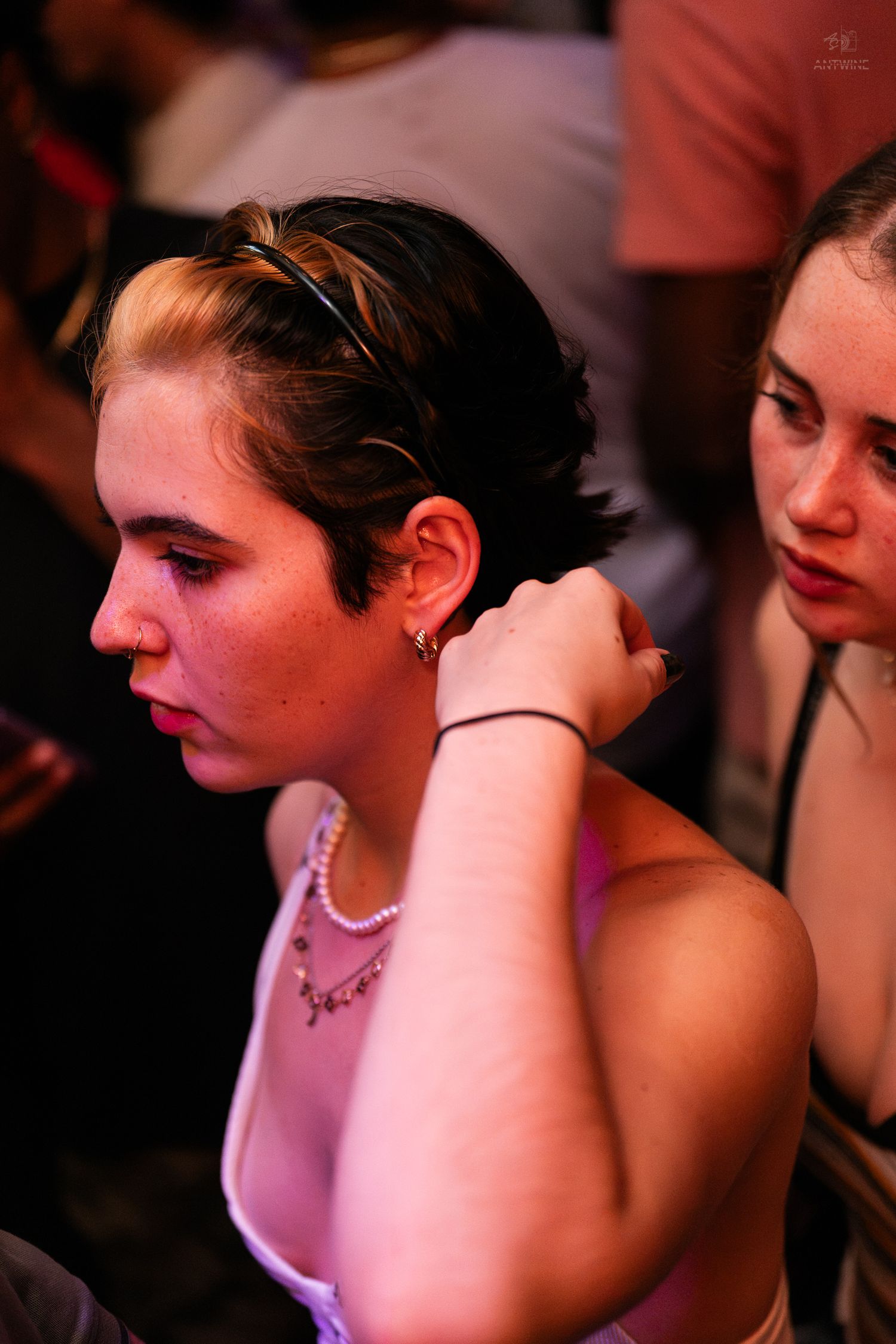 Young woman with short hair and pearl necklace at a dimly lit nightclub party.