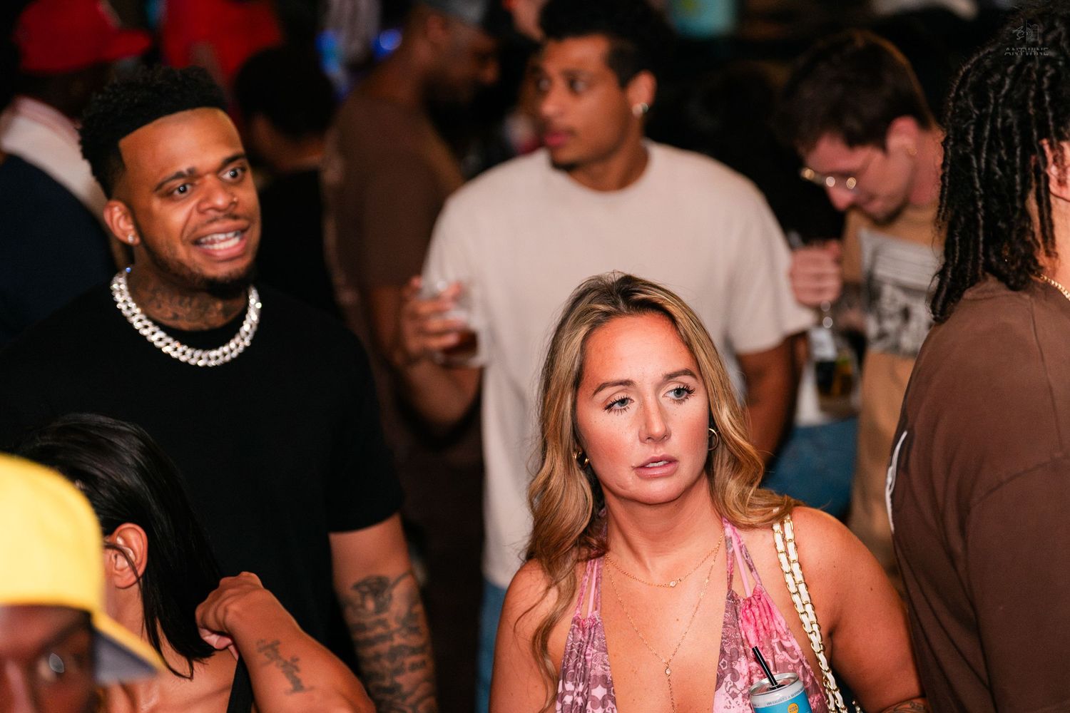 Man with chain necklace and woman in floral top at a crowded nightclub event.