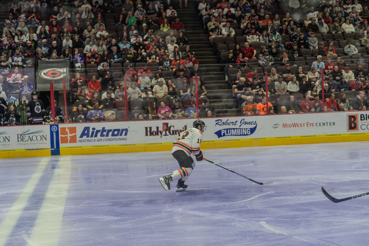 Hockey player in white Komets jersey skates across the ice during a professional indoor hockey game.