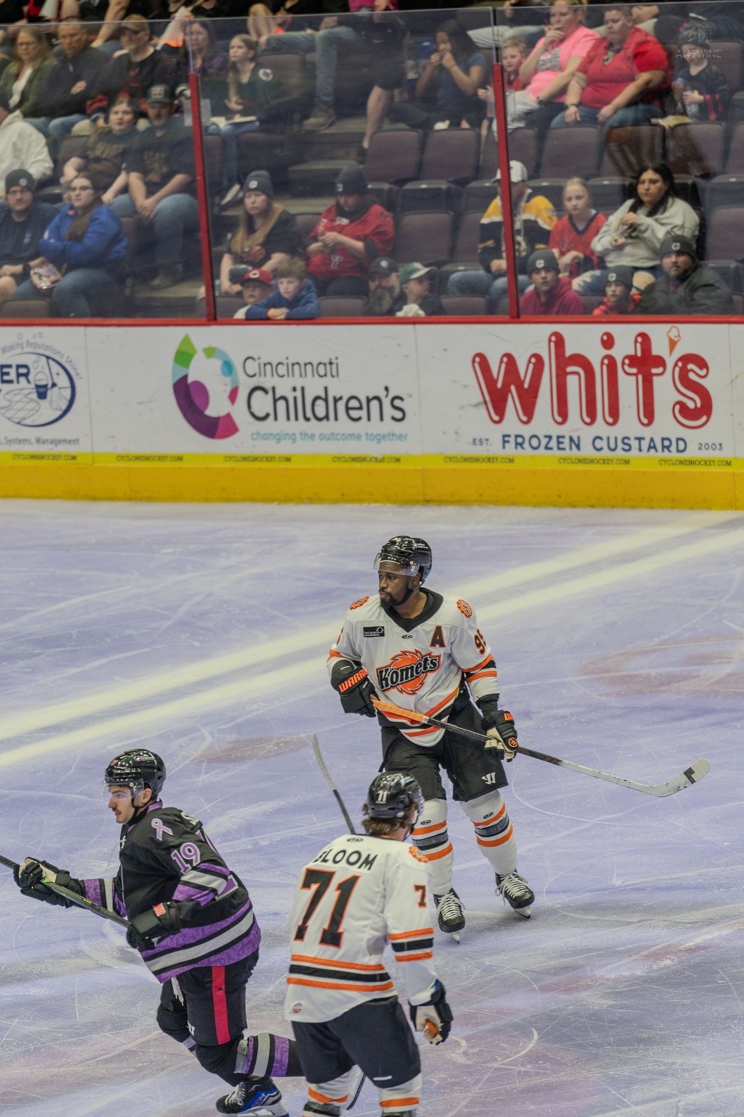 Minor league hockey players from two teams skate during gameplay with Cincinnati Childrens and Whits ads visible.