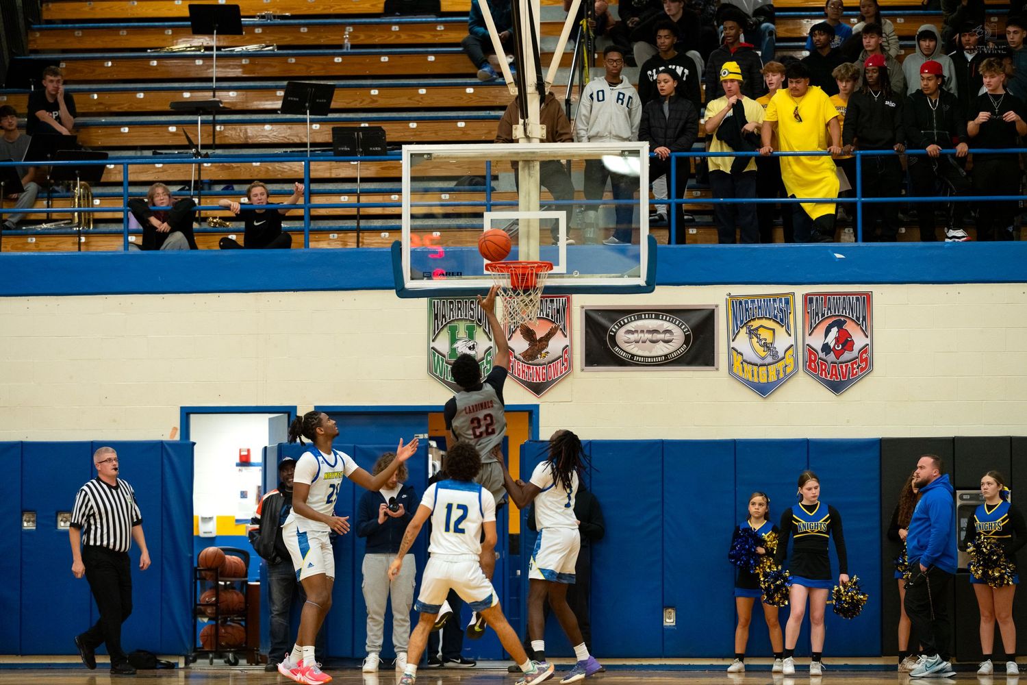 High school basketball players compete near the basket during an indoor game with fans in the stands.