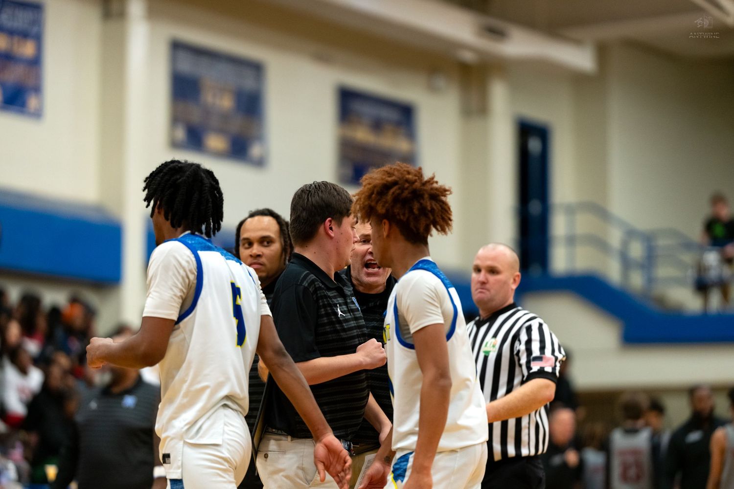 A coach passionately instructs players during a timeout at a high school basketball game.