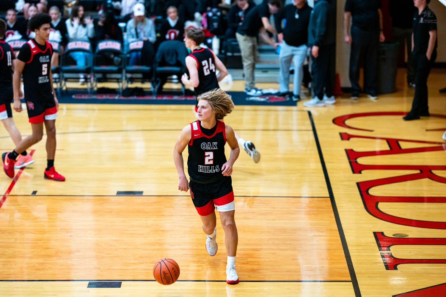 High school basketball player number 2 dribbles down the court during a game in a red gymnasium.