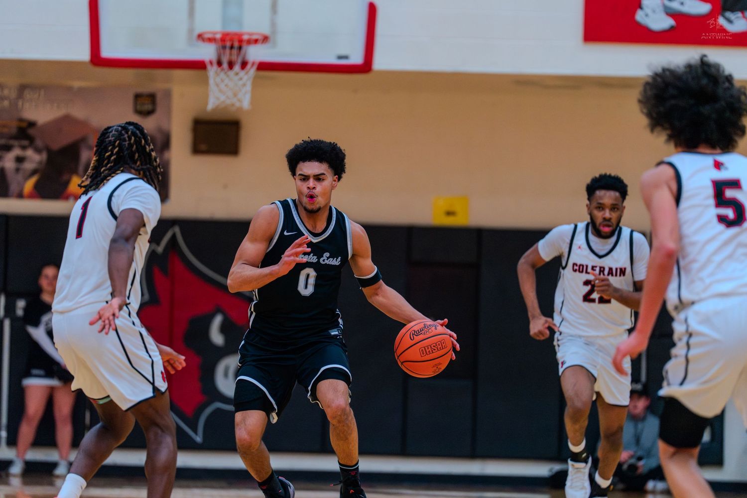 Lakota East player number 0 dribbles upcourt against Colerain defenders in a high school basketball game.