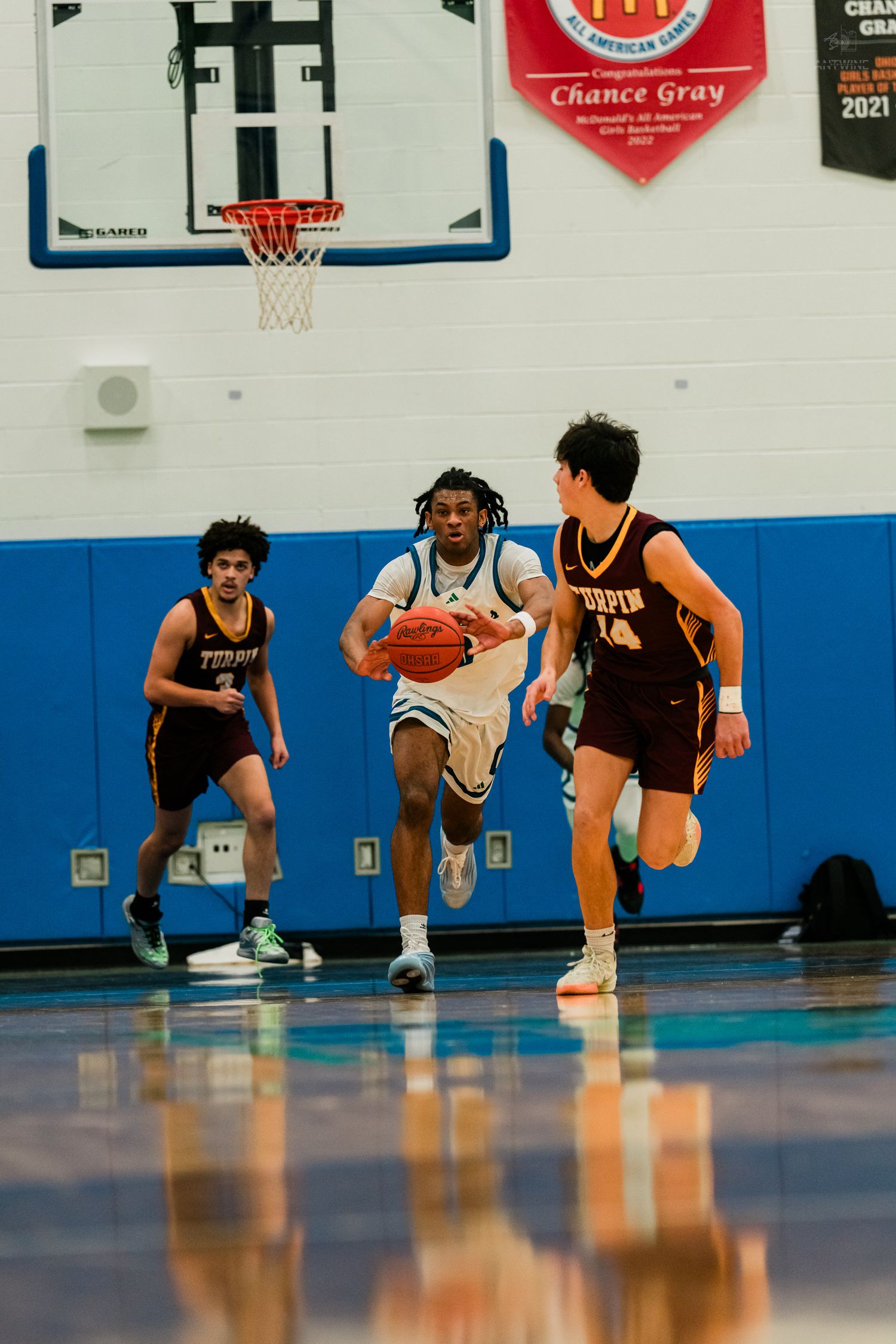 A Winton Woods player drives past two Turpin defenders on a fast break during a high school basketball game.