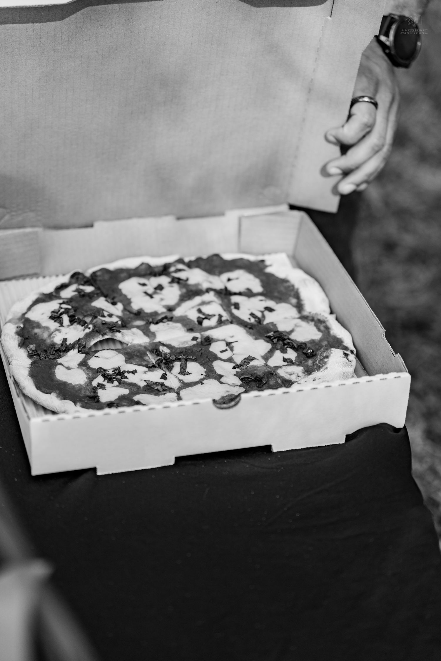 Black and white photo of a Margherita pizza in an open cardboard box held by a person.