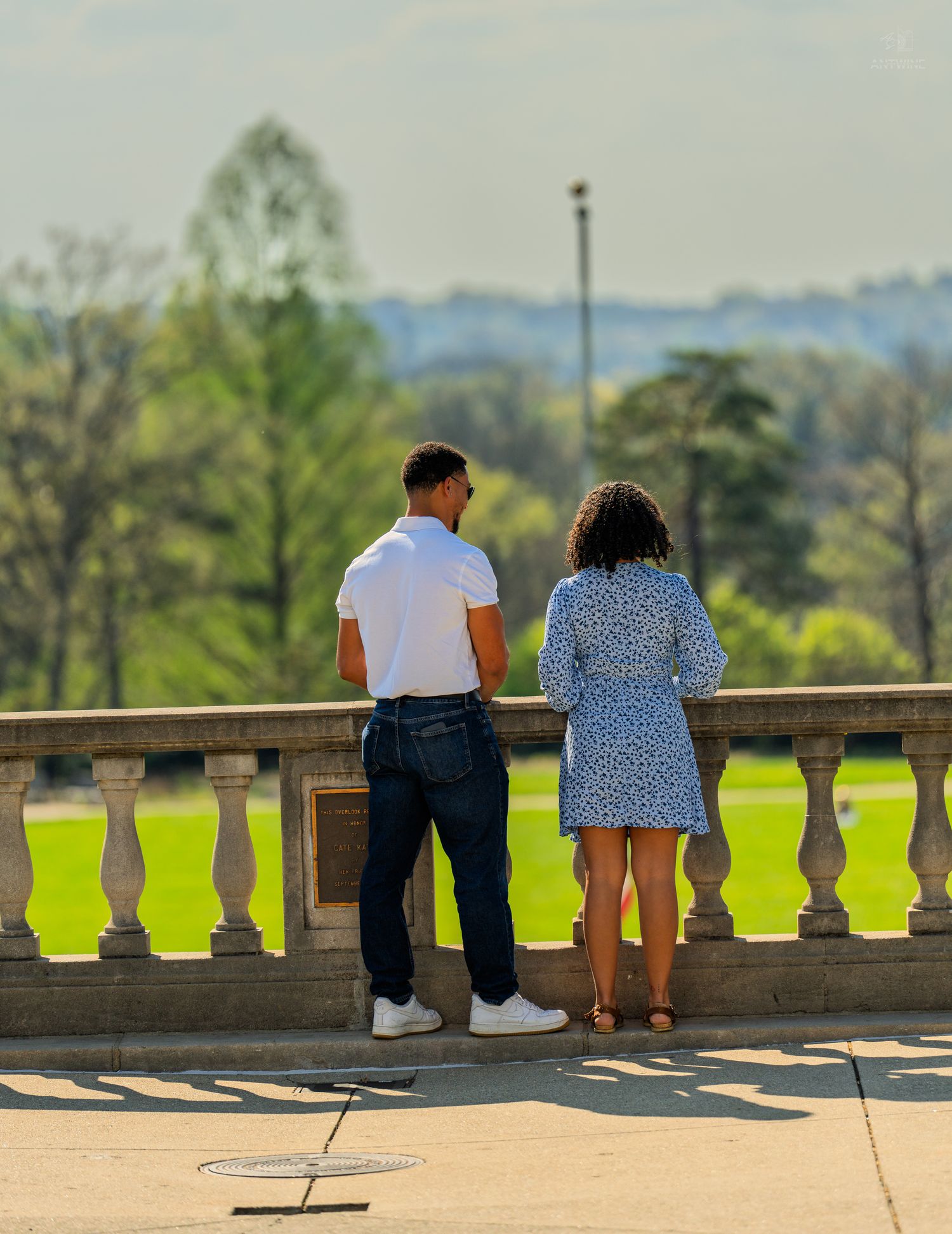 Couple in casual attire overlooking expansive green lawn from decorative stone terrace.