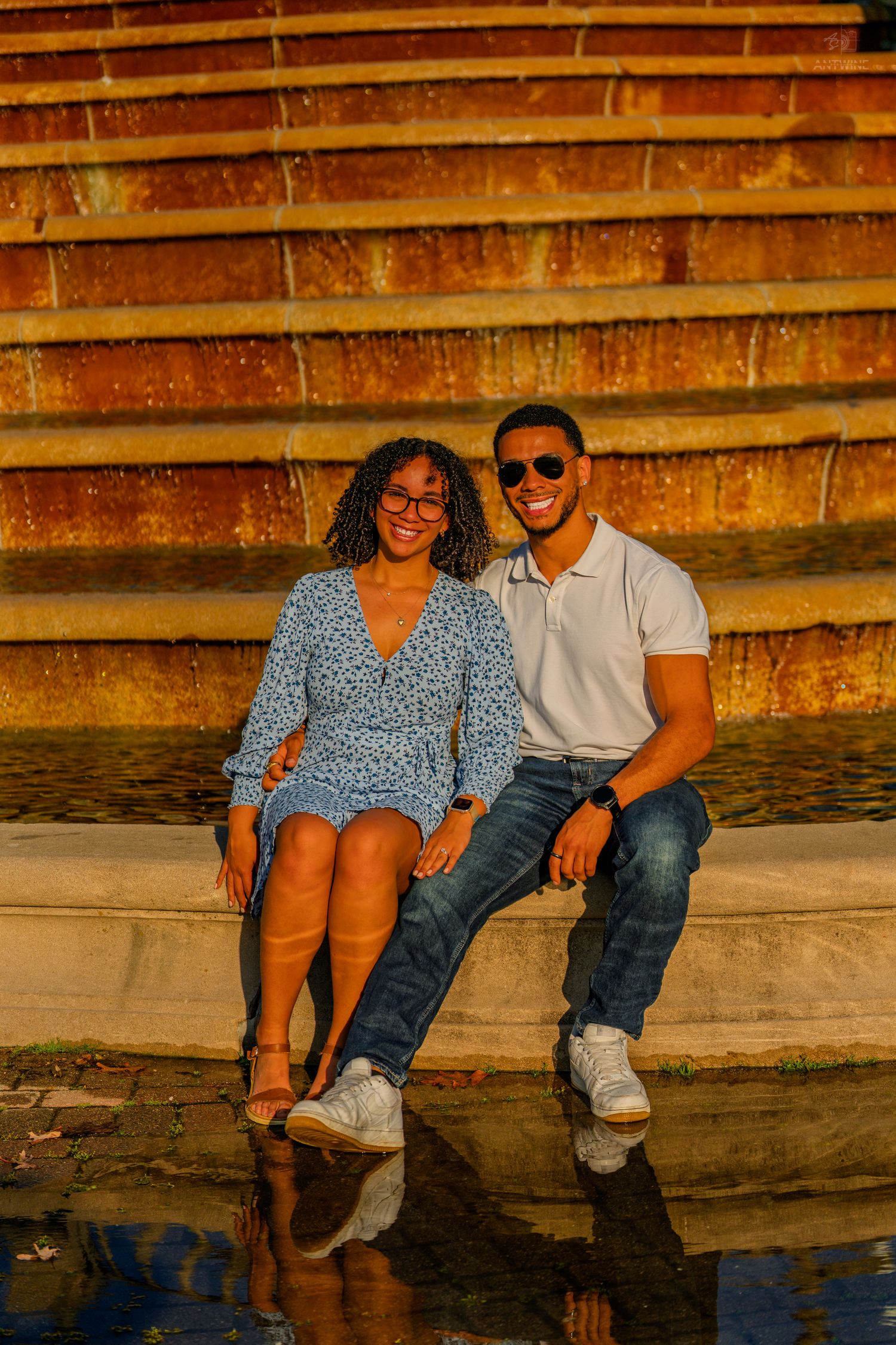 A joyful couple sits together on stone steps bathed in warm golden sunset light outdoors.