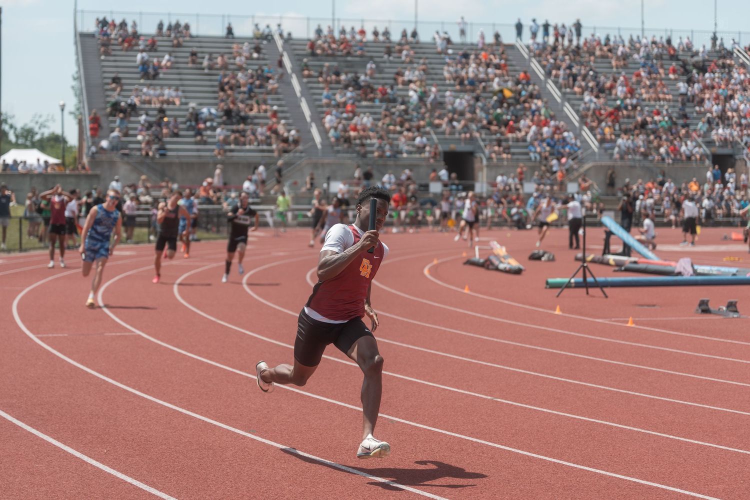 Athletes race on a red track at a well-attended outdoor track and field championship event.