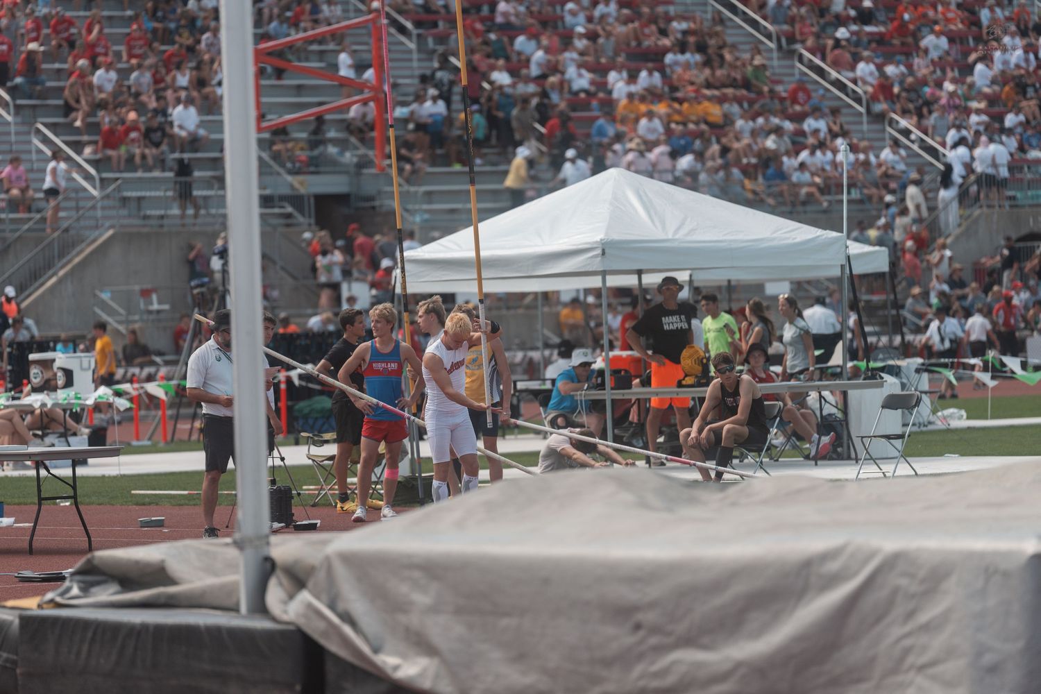 Pole vault athletes prepare to compete at a large outdoor track and field championship meet.