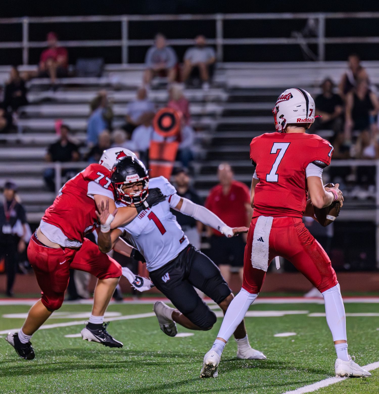 High school quarterback number 7 scrambles to avoid defender during intense football game action.