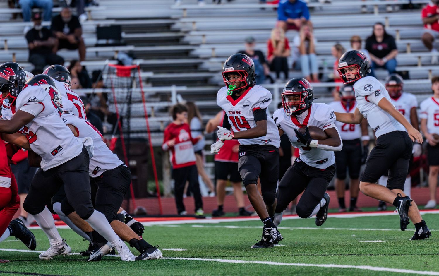 High school football player number 10 in red uniform runs with the ball during a night game.