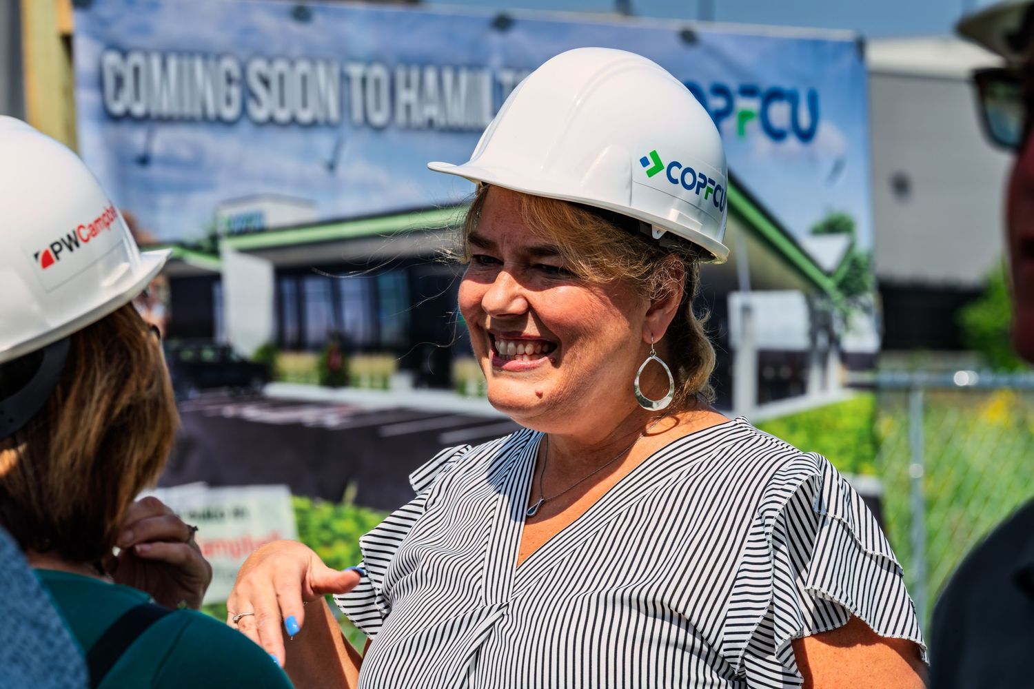 Smiling woman in COPFCU hard hat at coming soon to Hamilton groundbreaking event.