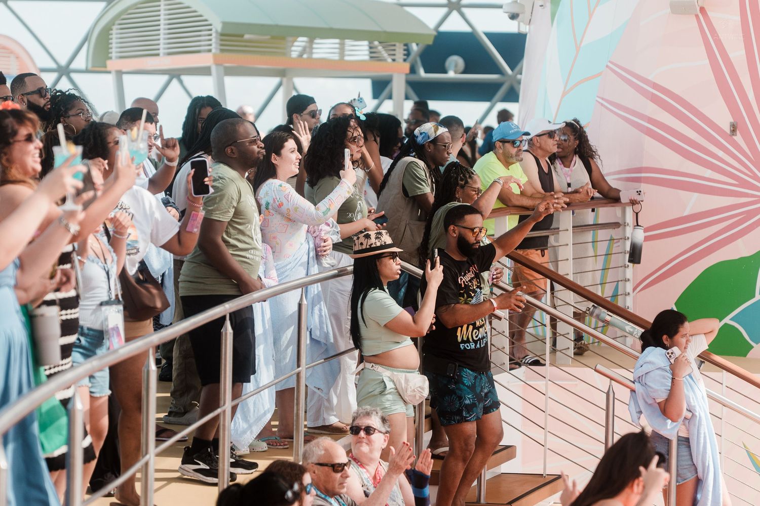 Excited cruise ship passengers taking photos from an upper deck railing.