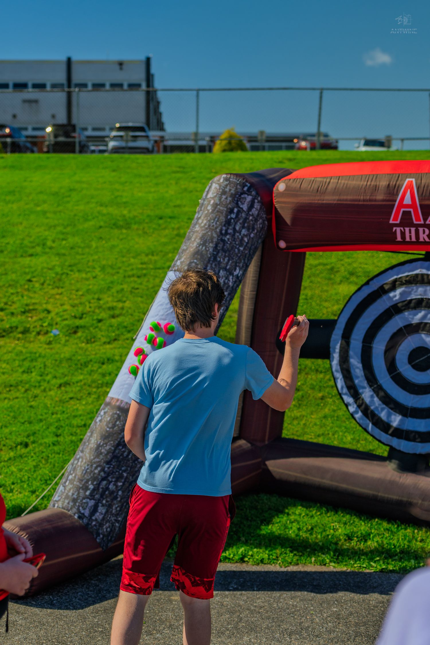 Boy in blue shirt playing inflatable axe throwing game outdoors on sunny day at a carnival event.