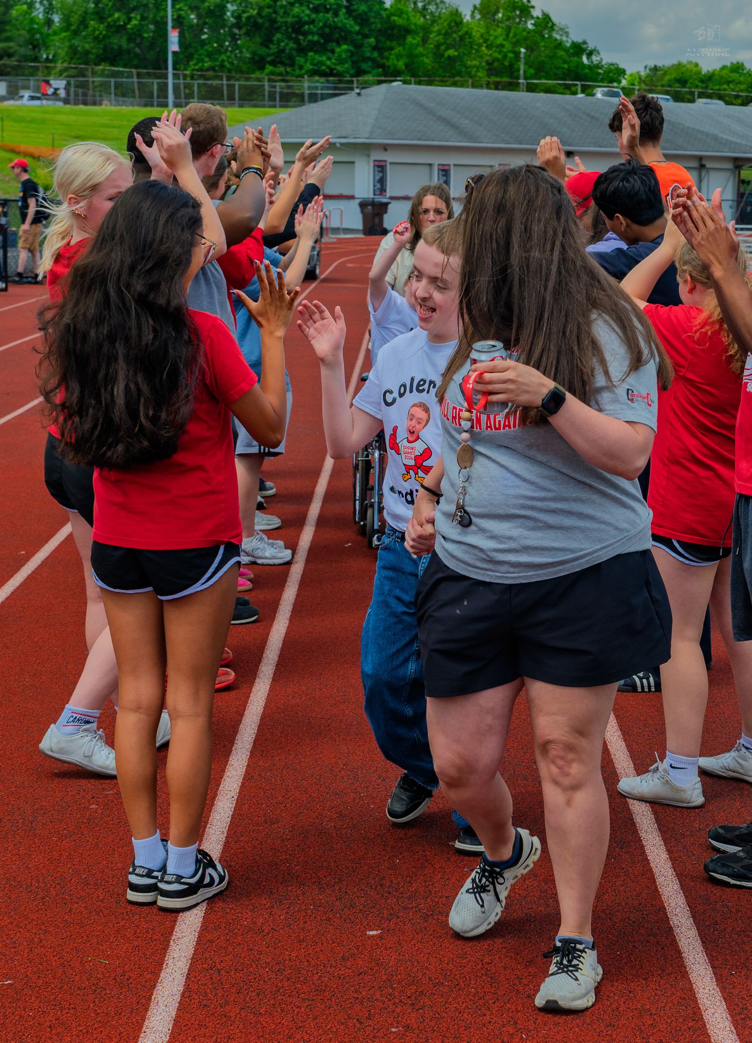 Students high-five athletes on a red track during a Special Olympics event at a school stadium.
