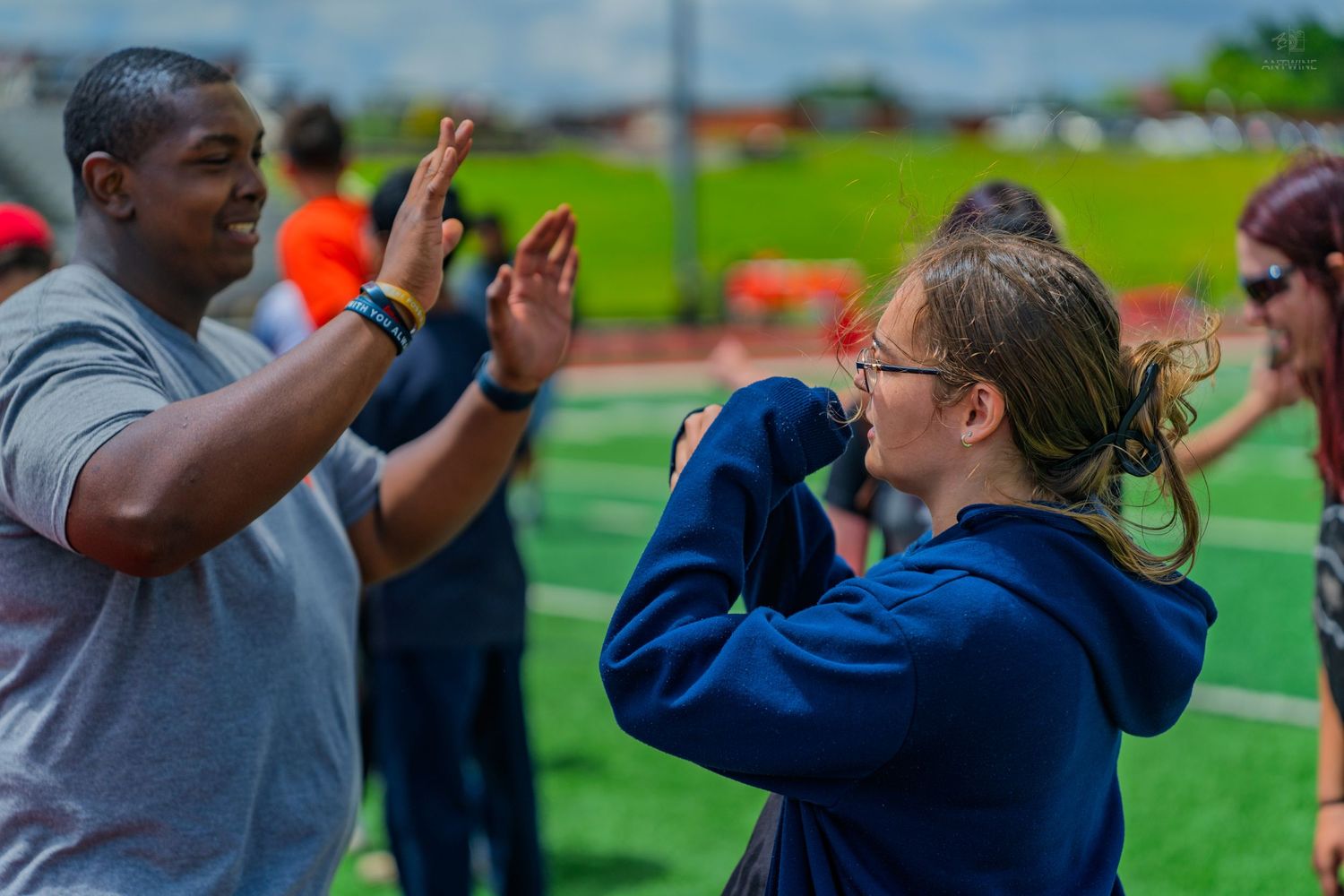 A man and woman high-fiving outdoors on a green sports field during a team activity event.