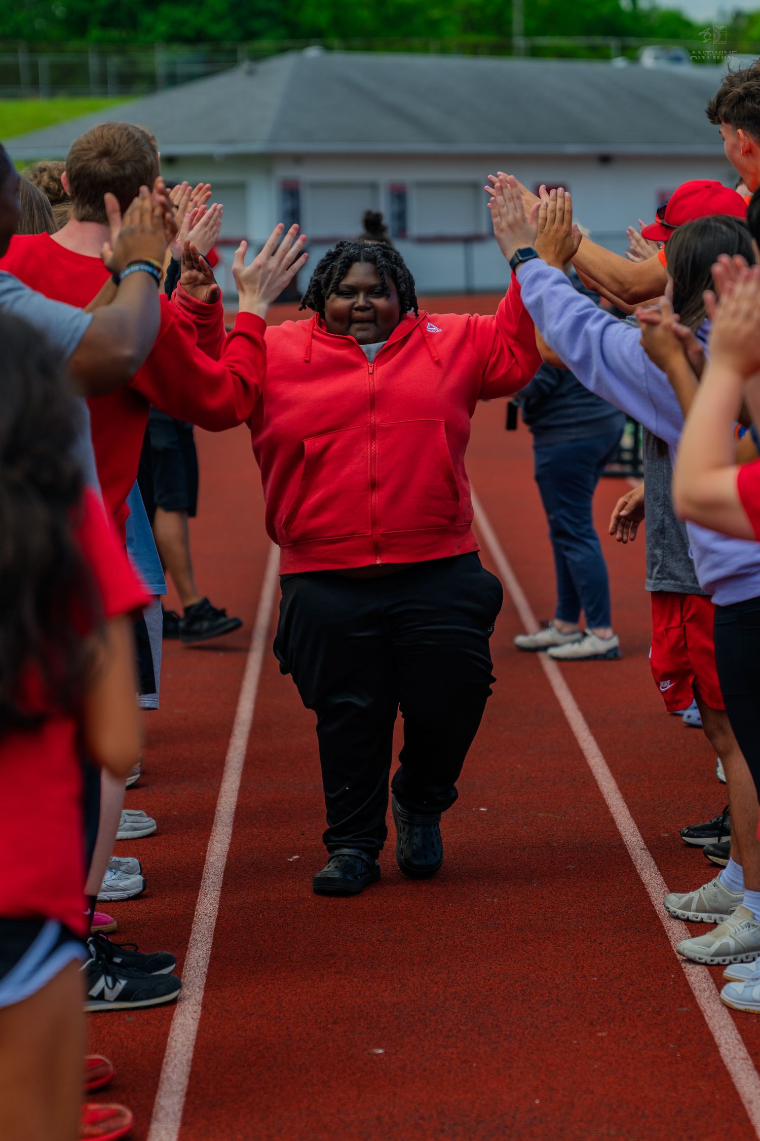 A student in a red jacket raises hands while walking through a high-five line on a school running track.