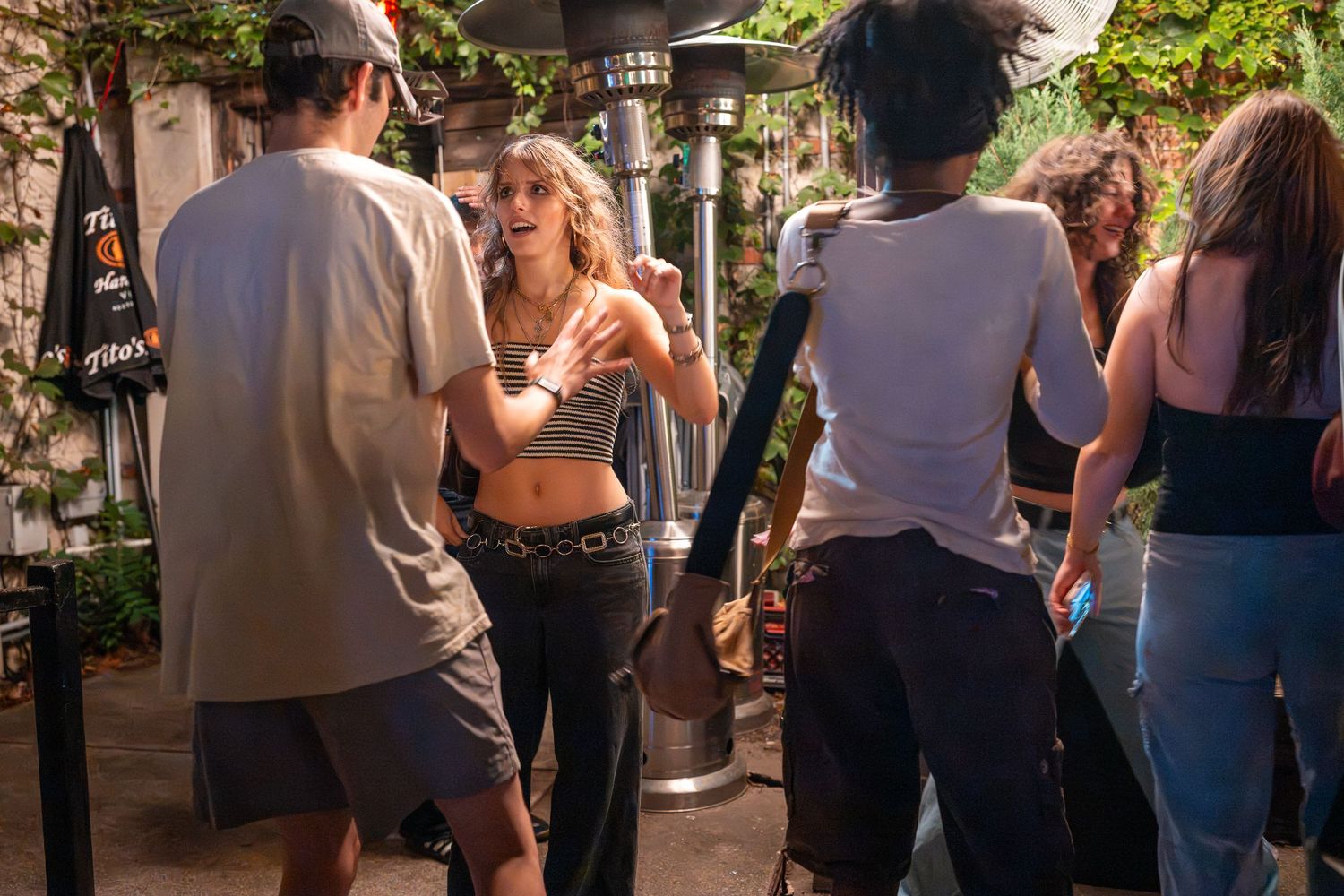 Young adults socializing and dancing outdoors at a lively evening party near patio heaters and lush greenery.