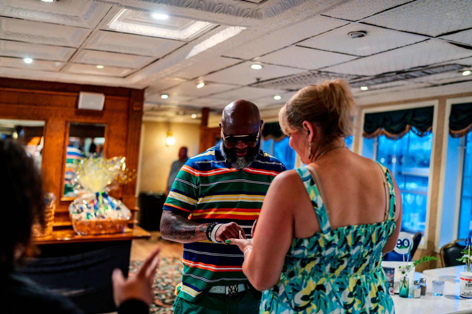 Two people conversing at an indoor gathering, man in striped shirt and woman in floral dress in elegant dining room.