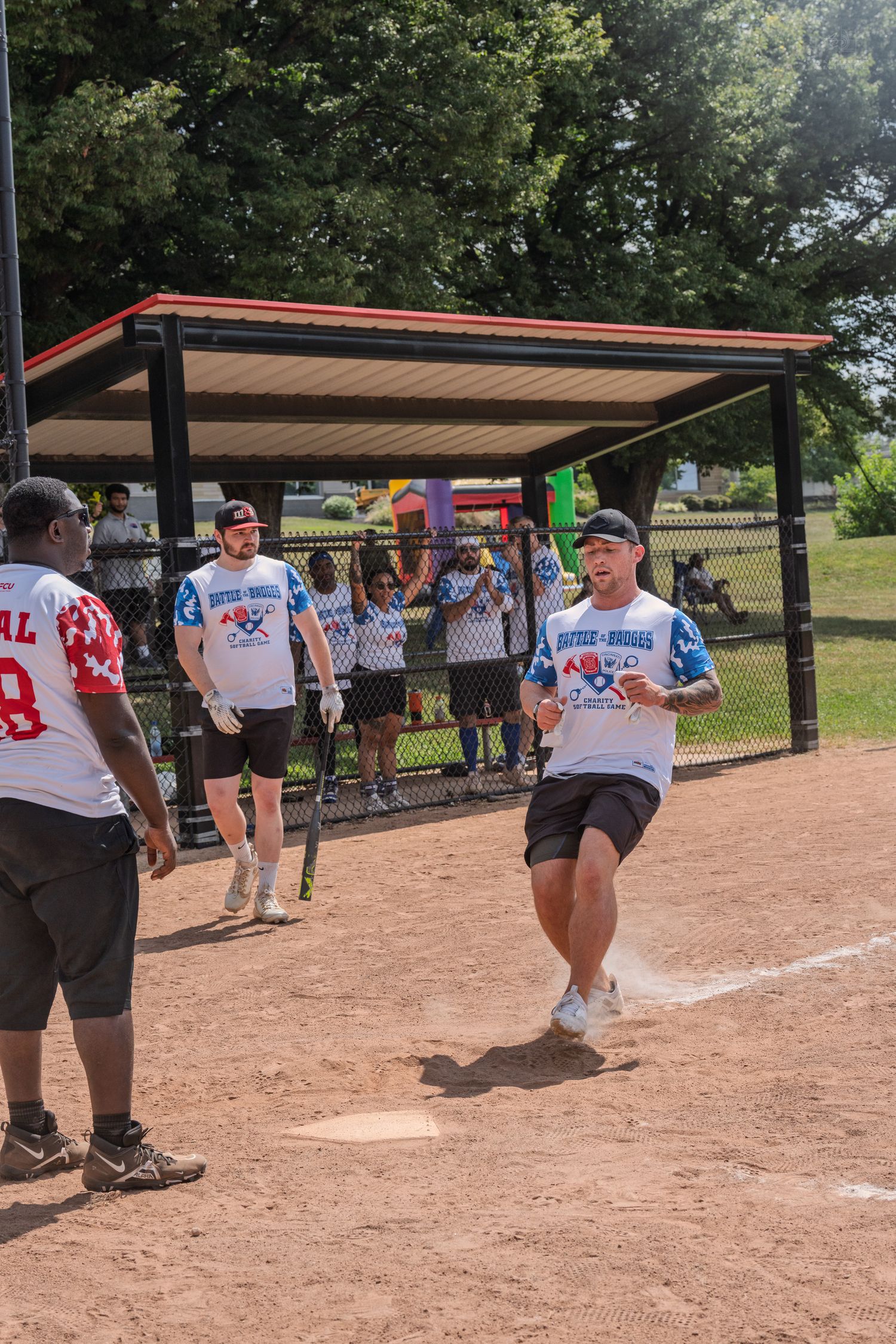 Softball players celebrating a run scored at home plate during a sunny outdoor charity game.