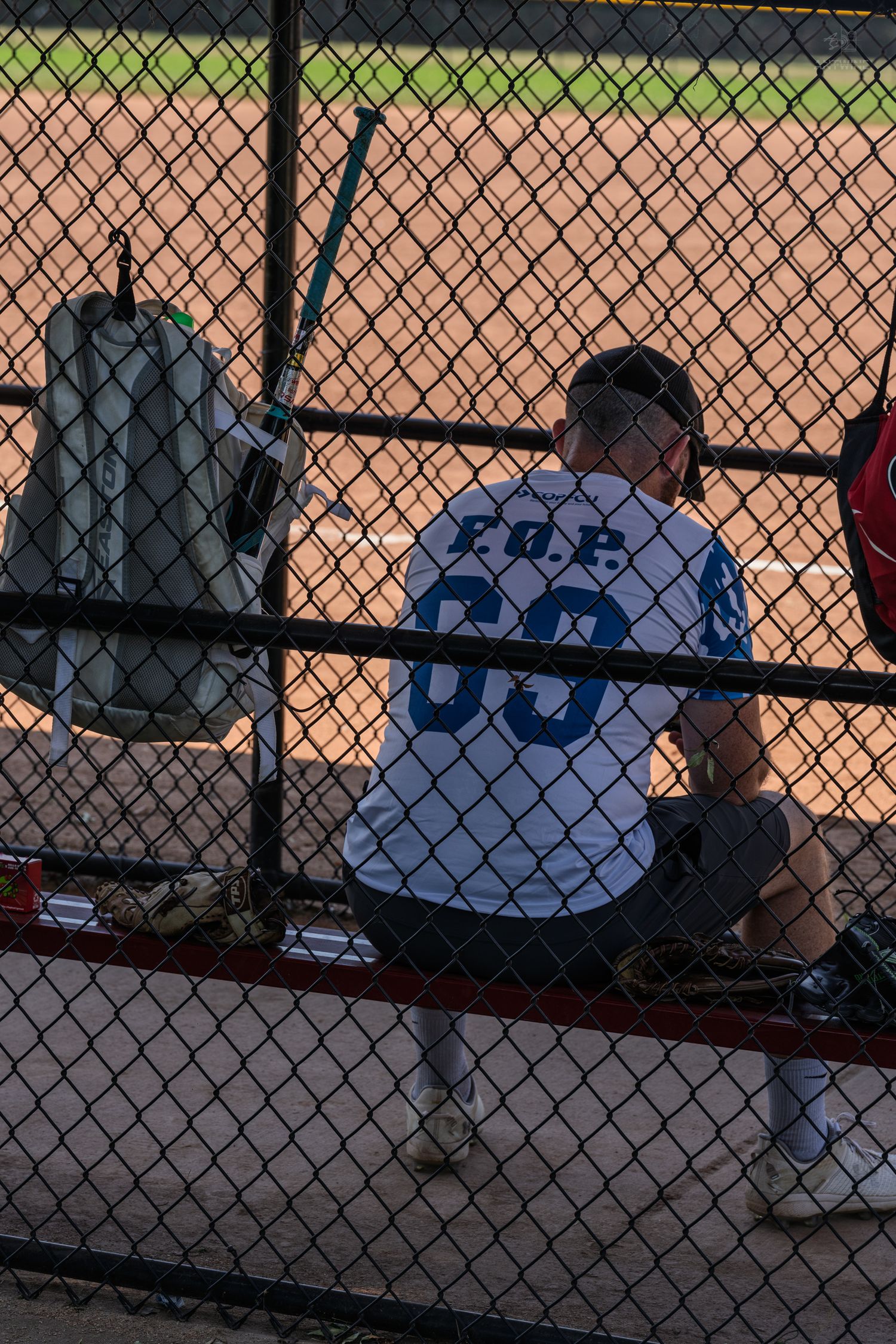 Baseball player in white jersey number 00 sits in dugout behind chain-link fence during a game.