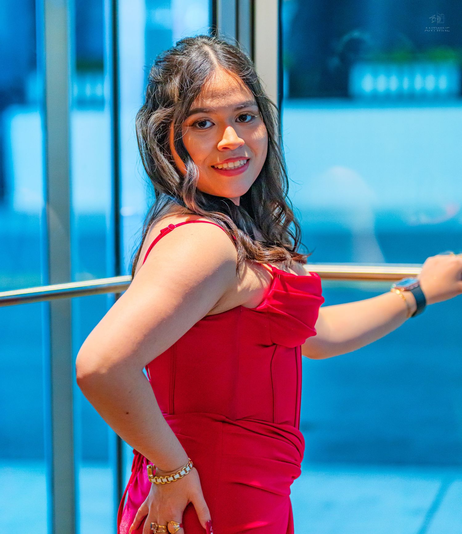 Young woman in red dress smiling and leaning on railing at formal venue.