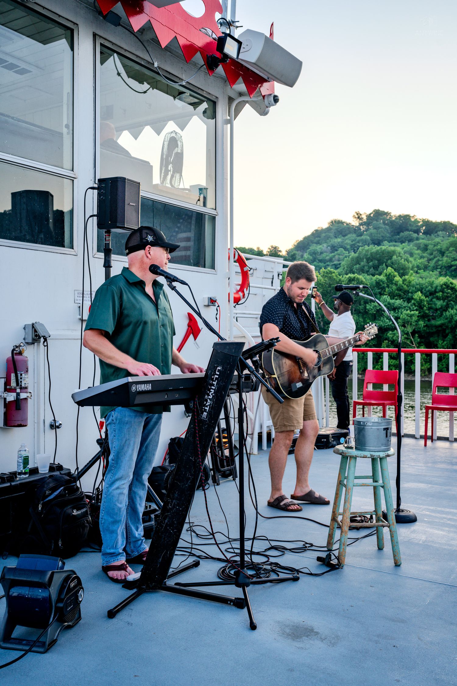 Live band performing outdoors on a boat deck at sunset with keyboard and guitar players on stage.