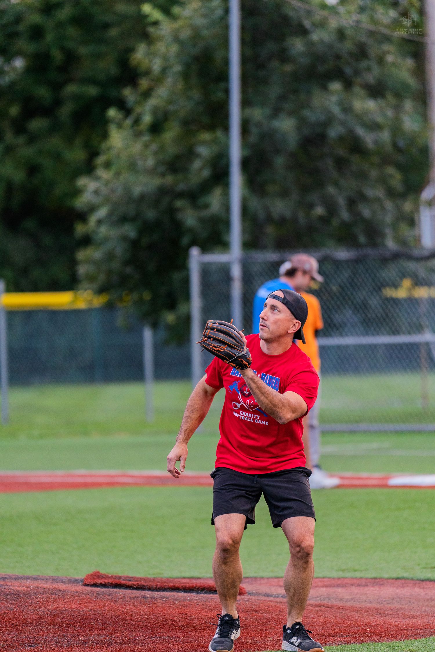 Man in red shirt catching a baseball with a glove on a field during a recreational softball game.