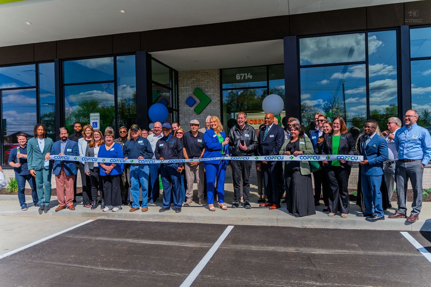 Group of people celebrating a ribbon cutting ceremony outside a modern commercial building on a sunny day.