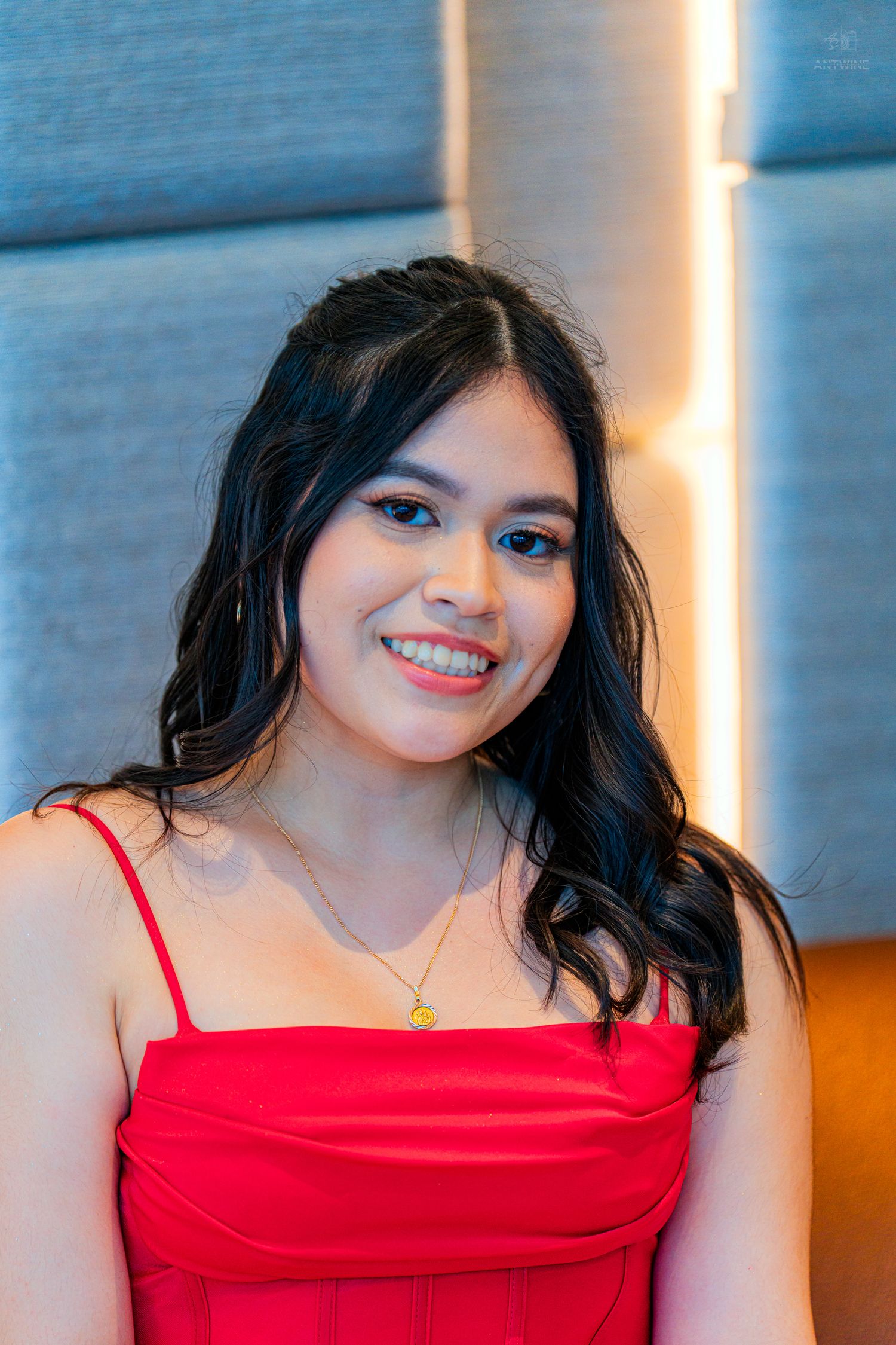 Young woman in red spaghetti strap dress smiling brightly against a modern backdrop.