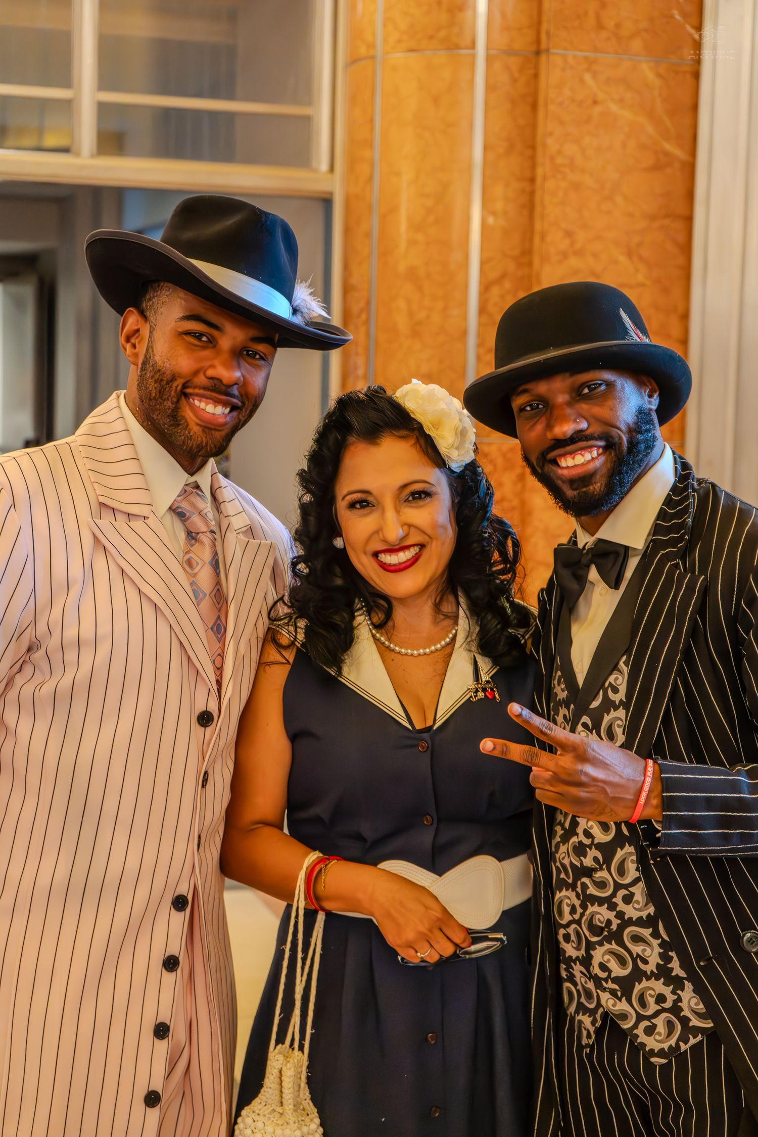 Three people in vintage 1940s-style attire, including pinstripe suits and hats, smiling at a formal event.
