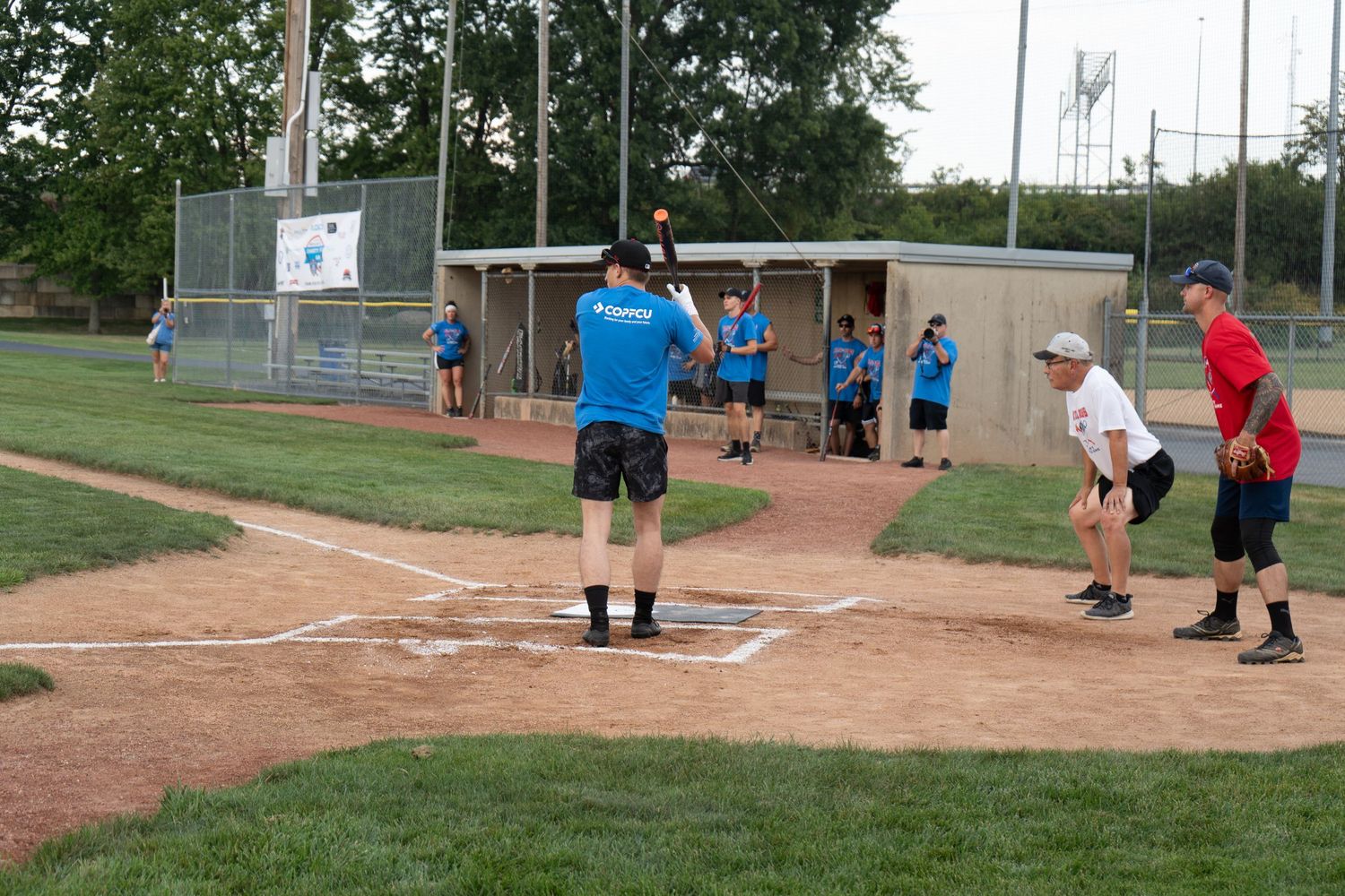 Adults playing recreational softball on a baseball diamond during a sunny day outdoor game.
