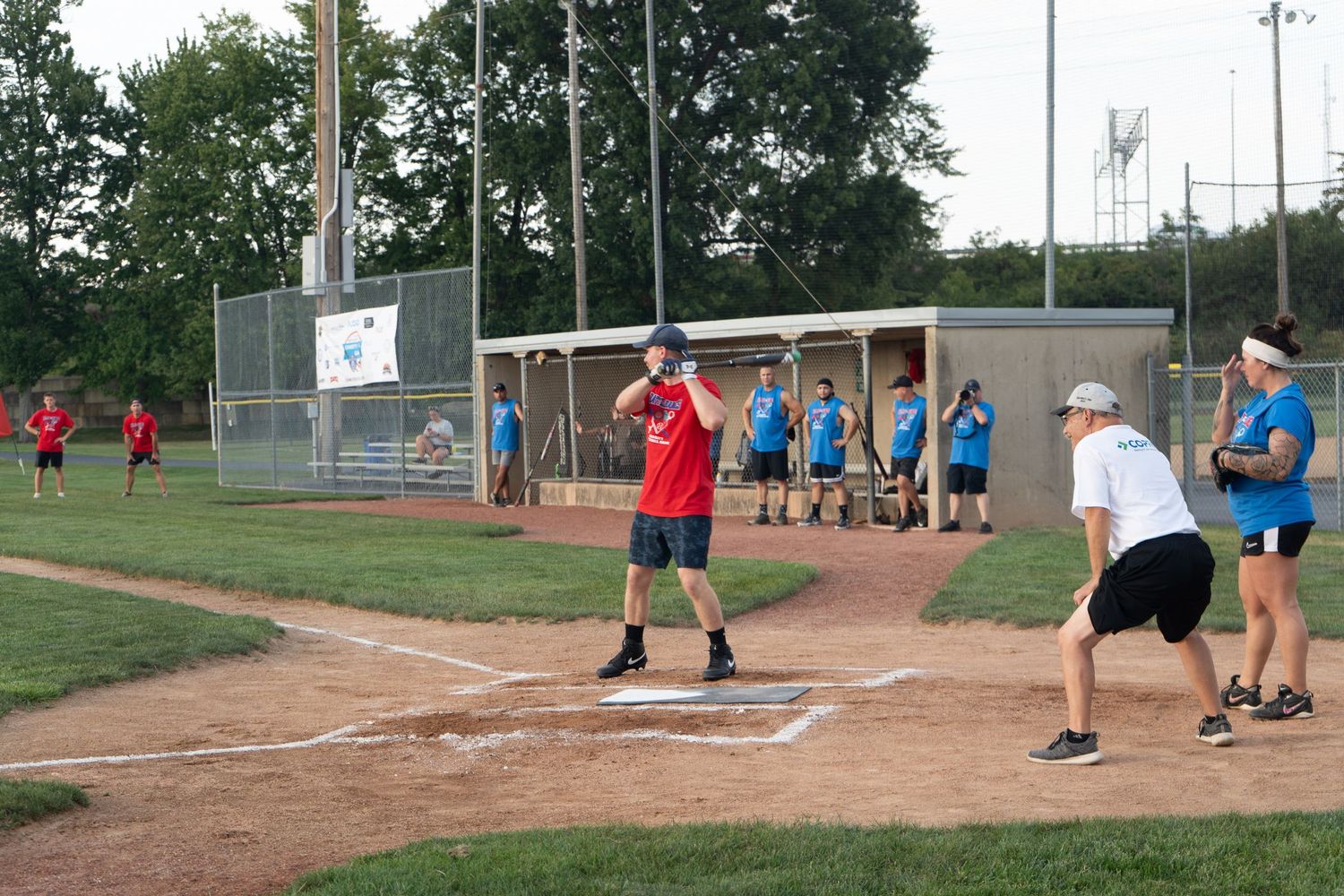 Adults playing recreational softball on a dirt diamond field during a summer evening game.